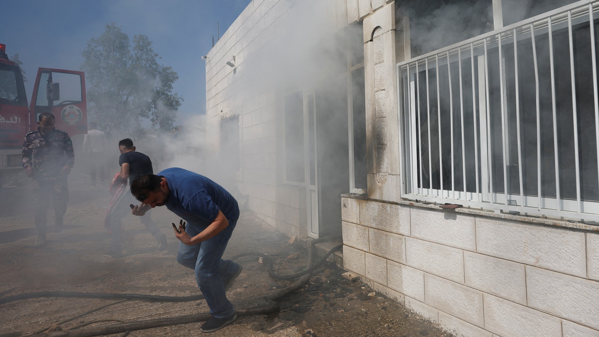A Palestinian man cowers as smoke leaves a building, after an attack by Israeli settlers in Turmusaya on 21 June (Reuters)
