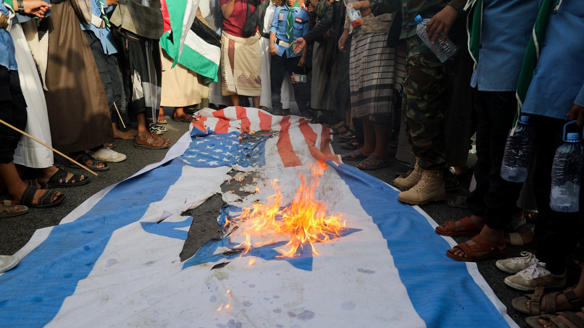 US and Israeli flags burn as Houthi supporters rally to show support to Palestinian factions, in Sanaa, 7 October (Reuters)