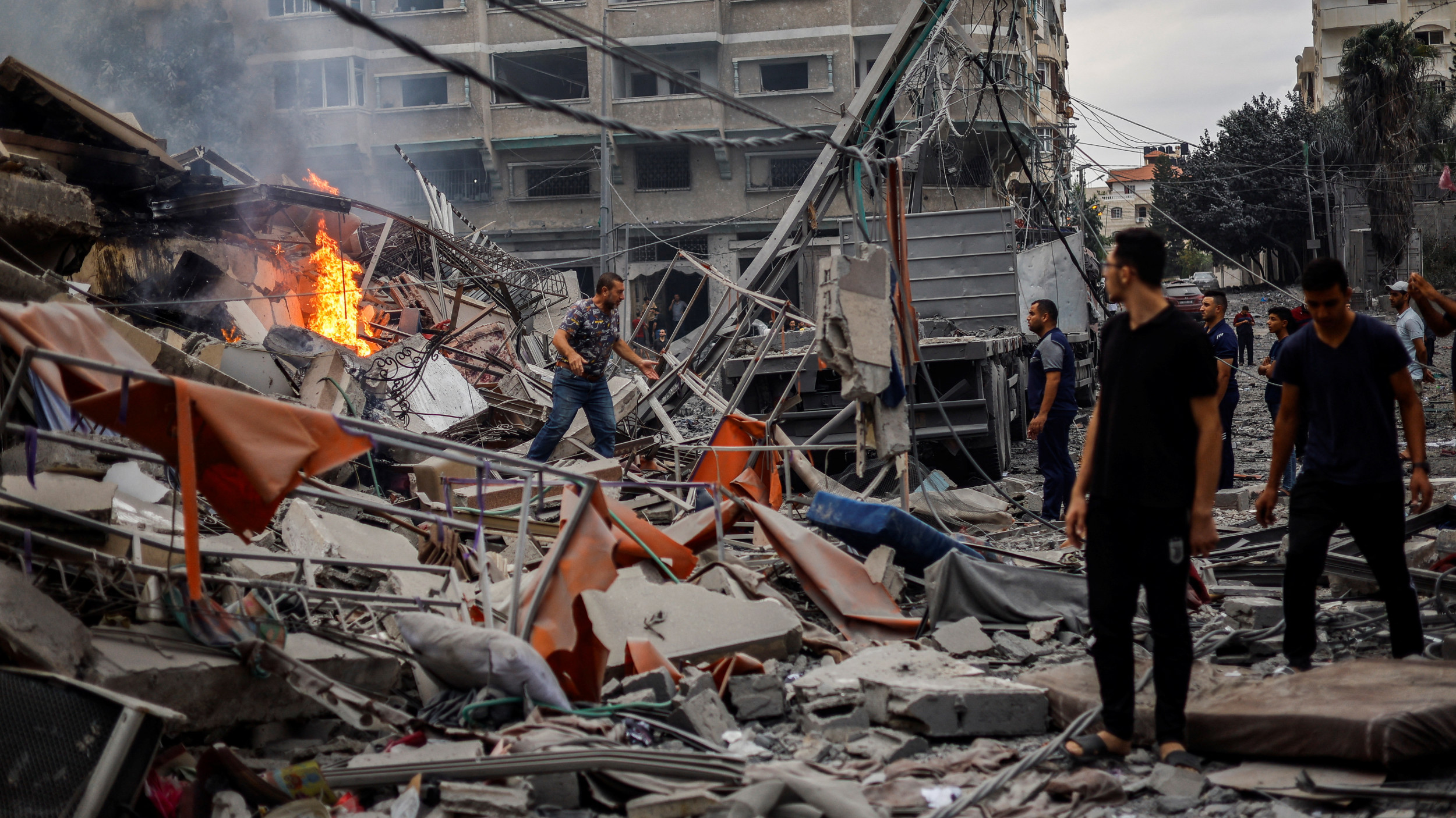 Des Palestiniens regardent un incendie brûler parmi les décombres d’un immeuble résidentiel endommagé, à la suite de frappes israéliennes, dans la ville de Gaza, le 10 octobre 2023 (Reuters)