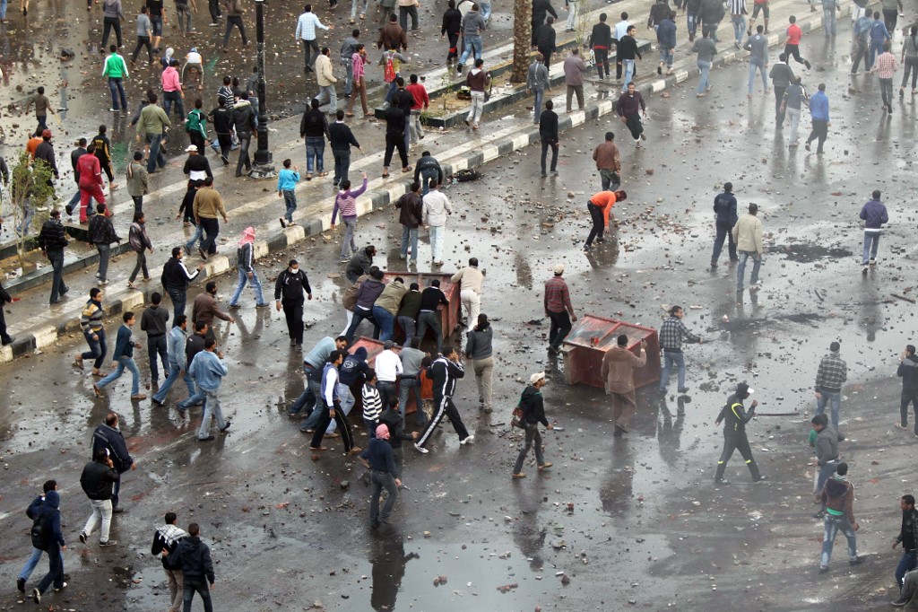 Protesters in Suez, some using upturned garbage skips for cover, call for the fall of Hosni Mubarak on 27 January 2011 (AFP)