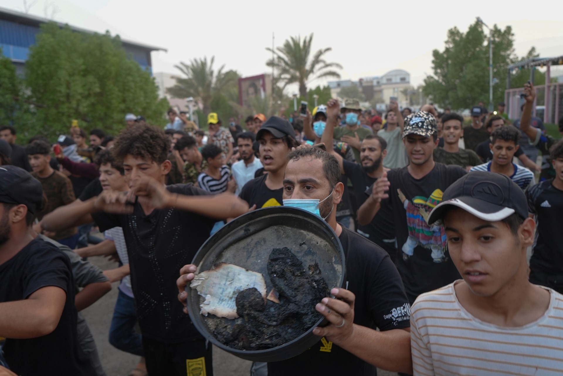 As Iraqis protest in Nasiriyah, one man holds a dish containing burnt remains of a victim (MEE/Azhar Al-Rubaie)