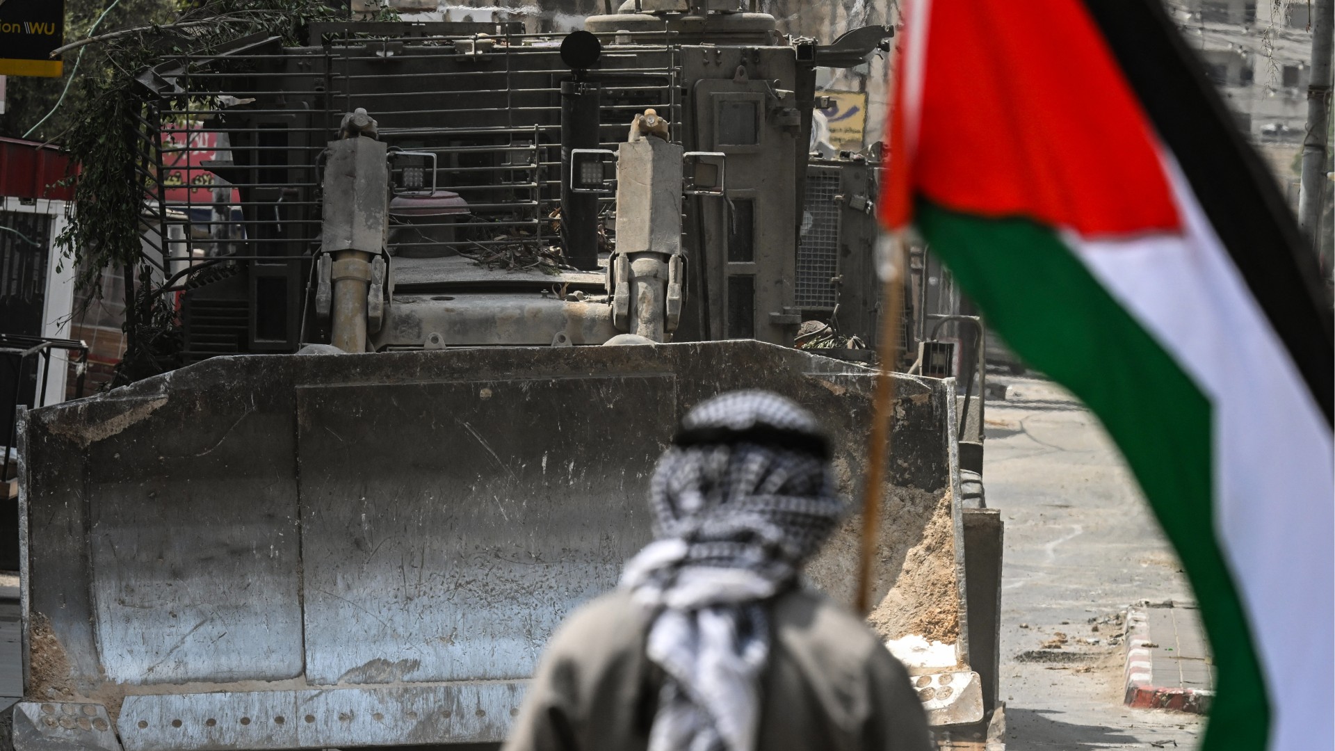 A Palestinian man holding a national flag stands in front of a bulldozer during an Israeli raid in the centre of Jenin in the occupied West Bank on September 2, 2024-afp