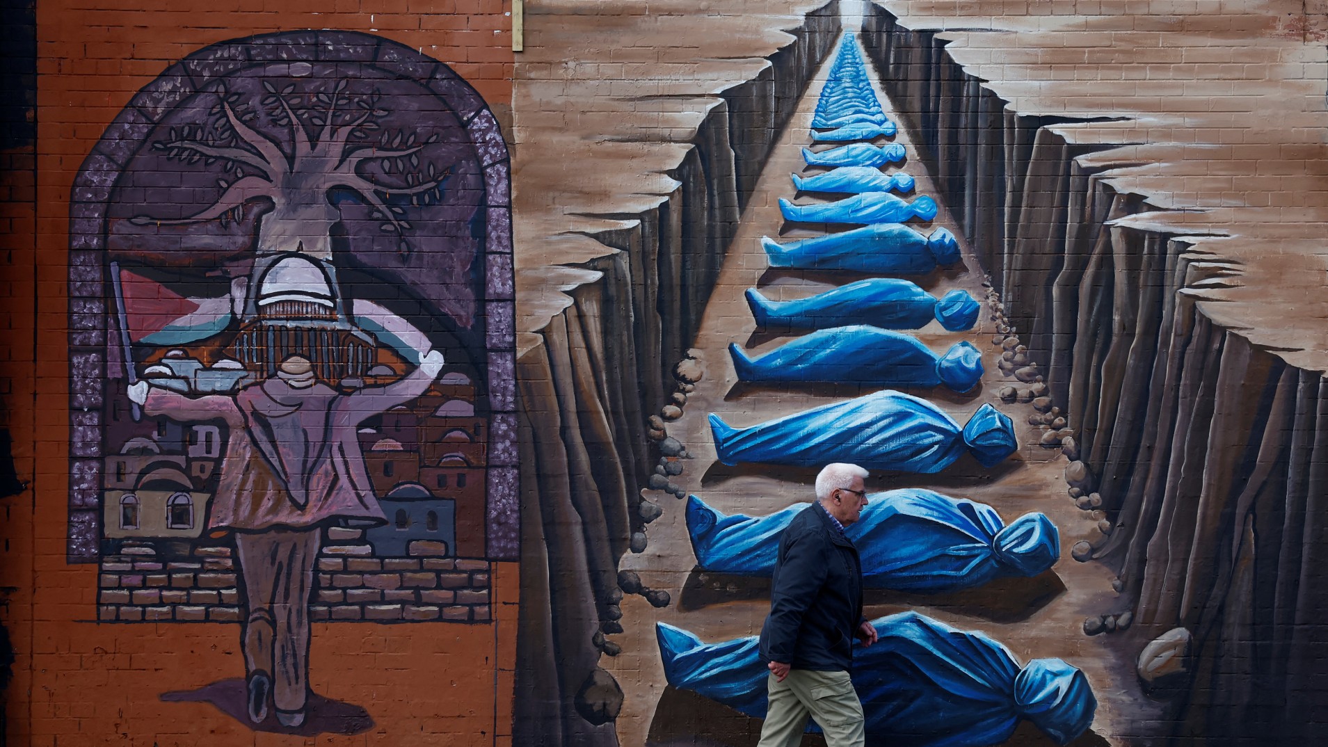 A man walks past pro-Palestinian murals on the International Wall in support of Gaza in Belfast, Northern Ireland on 9 March, 2024 (Reuters)