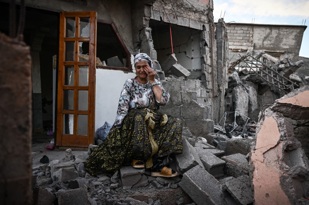 A survivor of the 8 September earthquake sits on the rubble of her damaged house, in the mountain village of Moulay Brahim in al-Haouz province in central Morocco, 10 September 2023 (AFP) 
