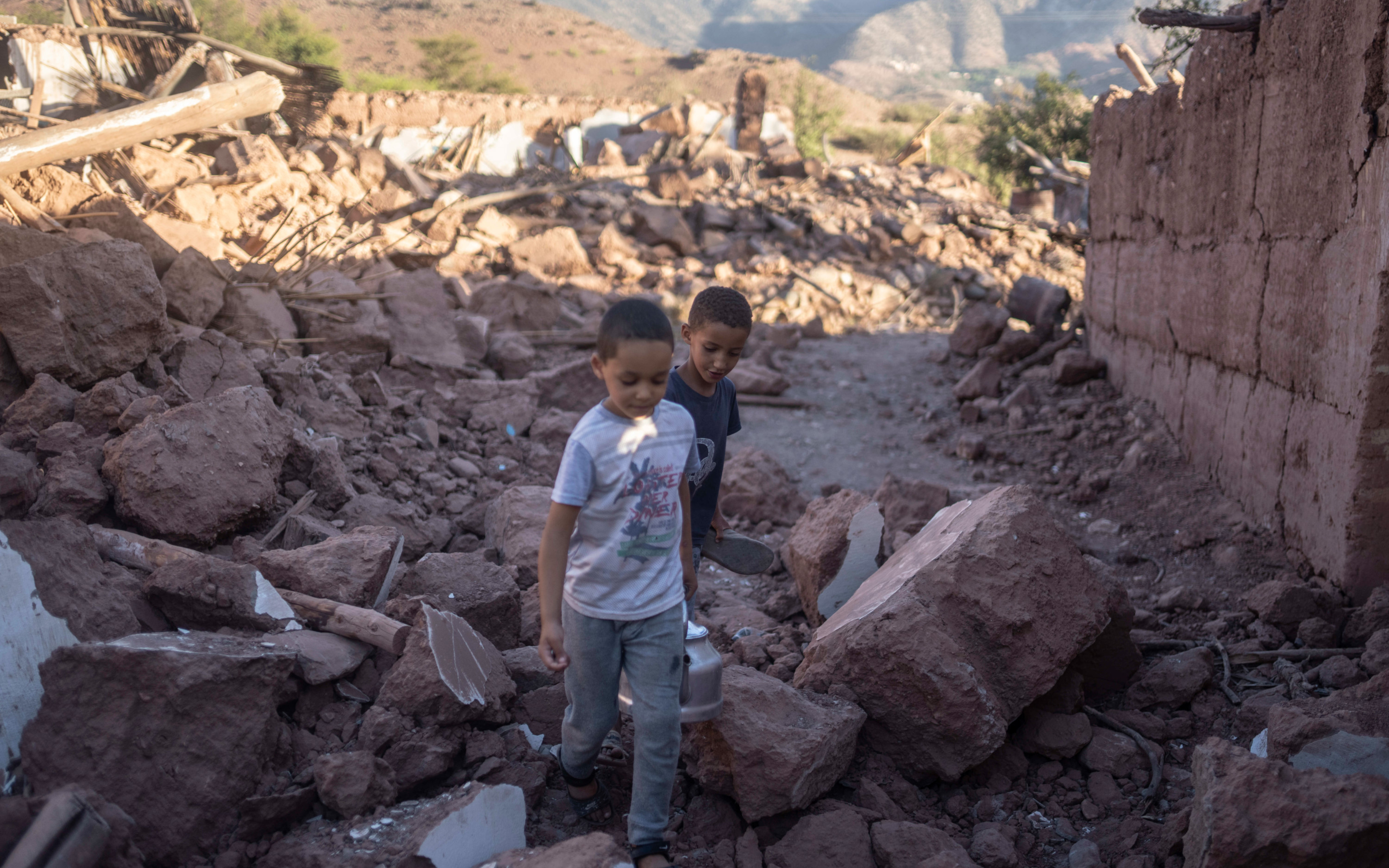 Moroccan boys walk amidst the rubble of their home which was damaged by the earthquake, in Ijjoukak village, near Marrakech on 9 September 2023 (AP)