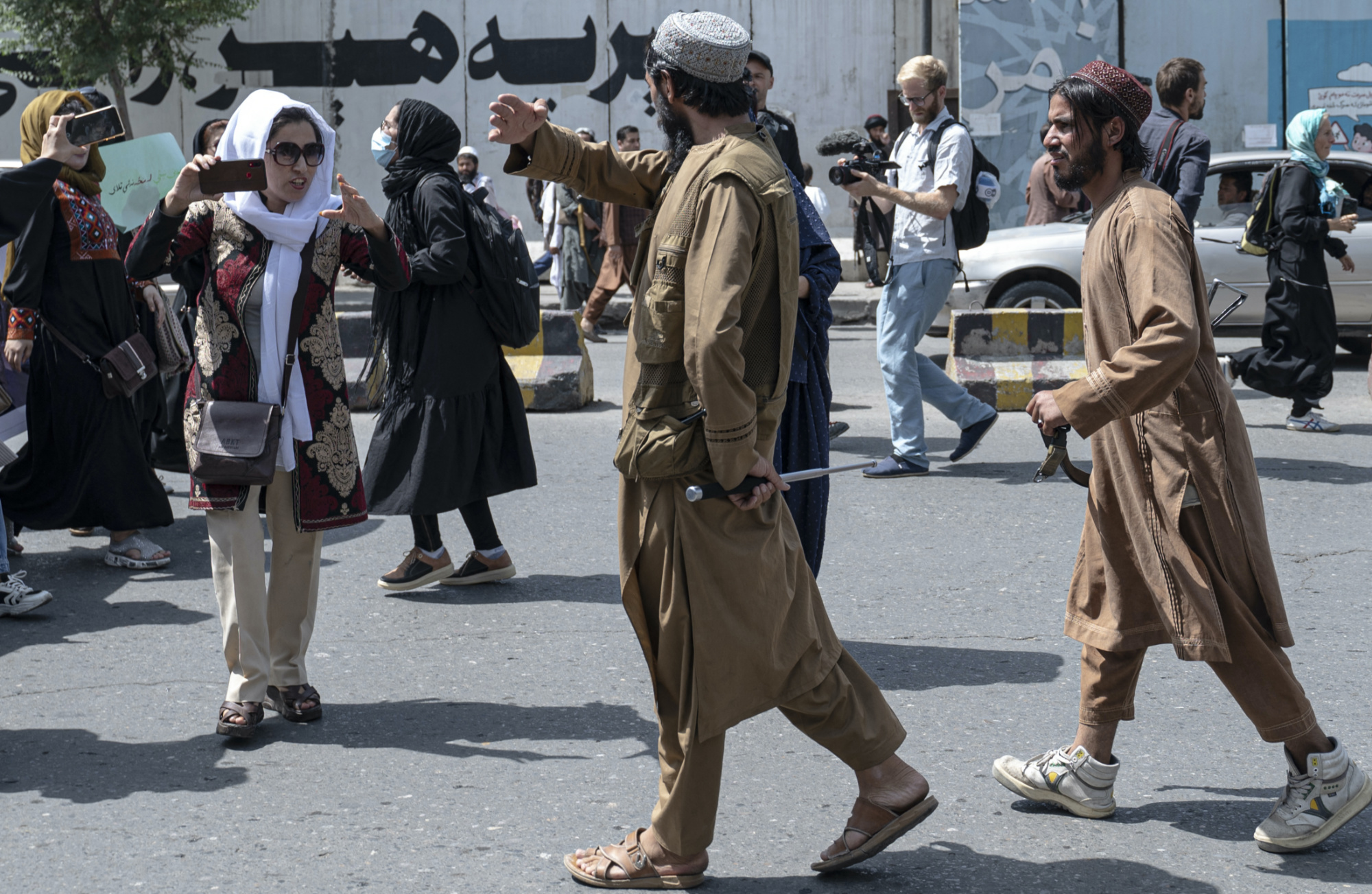 Taliban fighters walk as they fire into the air to disperse Afghan women protesters in Kabul on 13 August 2022 (AFP)