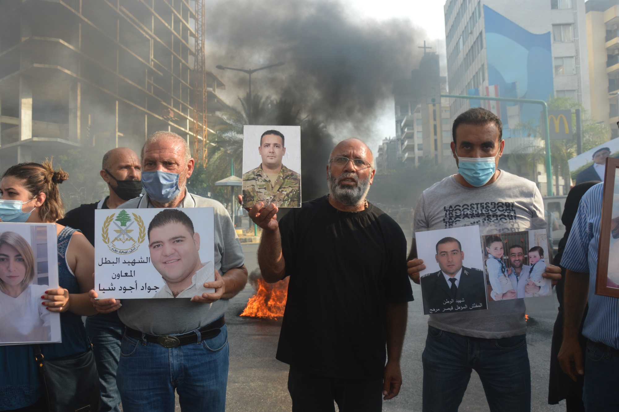 Families of the victims of Beirut port explosion hold framed pictures of their loved as tyres burn during a demonstration near the Ministry of Justice on 14 July 2021 (MEE/Dario Sabaghi)