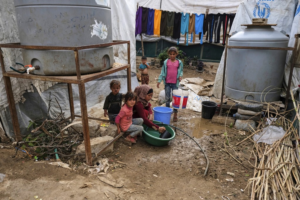 Children sit by as a woman washes dishes in a plastic basin outside a tent at a makeshift camp for Syrian refugees in Talhayat in the Akkar district in north Lebanon, 26 October 2022 (AFP)