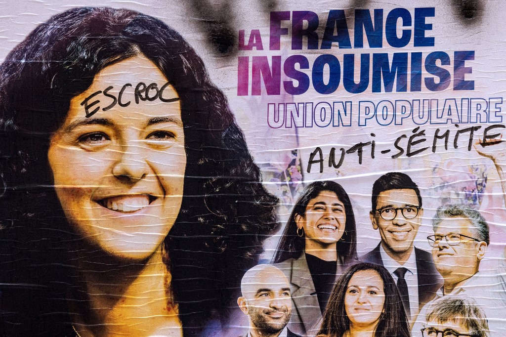 A European elections campaign poster of France Unbowed (LFI) with lead candidate Manon Aubry (on the left) and seventh candidate Rima Hassan (first on the right) with graffiti on it reading in French "Scammer" and "Anti-Semitic", in Paris on 3 June 2024 (Joel Saget/AFP)