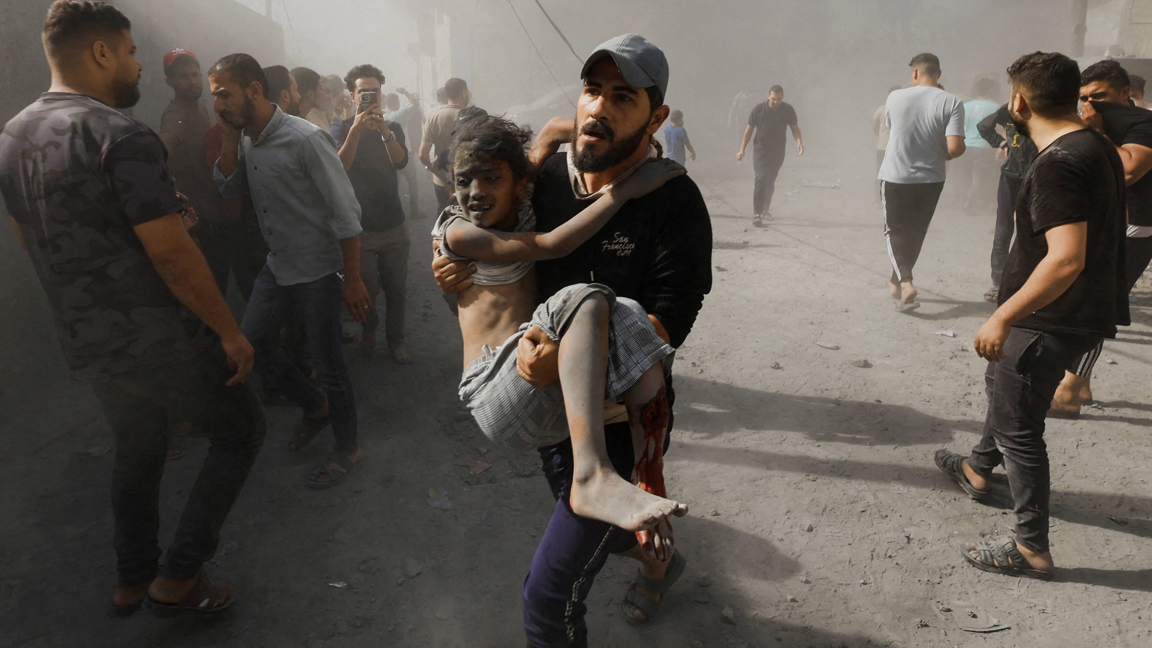 A Palestinian man carries a wounded child at the site of Israeli strikes on houses in Khan Younes in the southern Gaza, 26 October 2023 (Reuters)