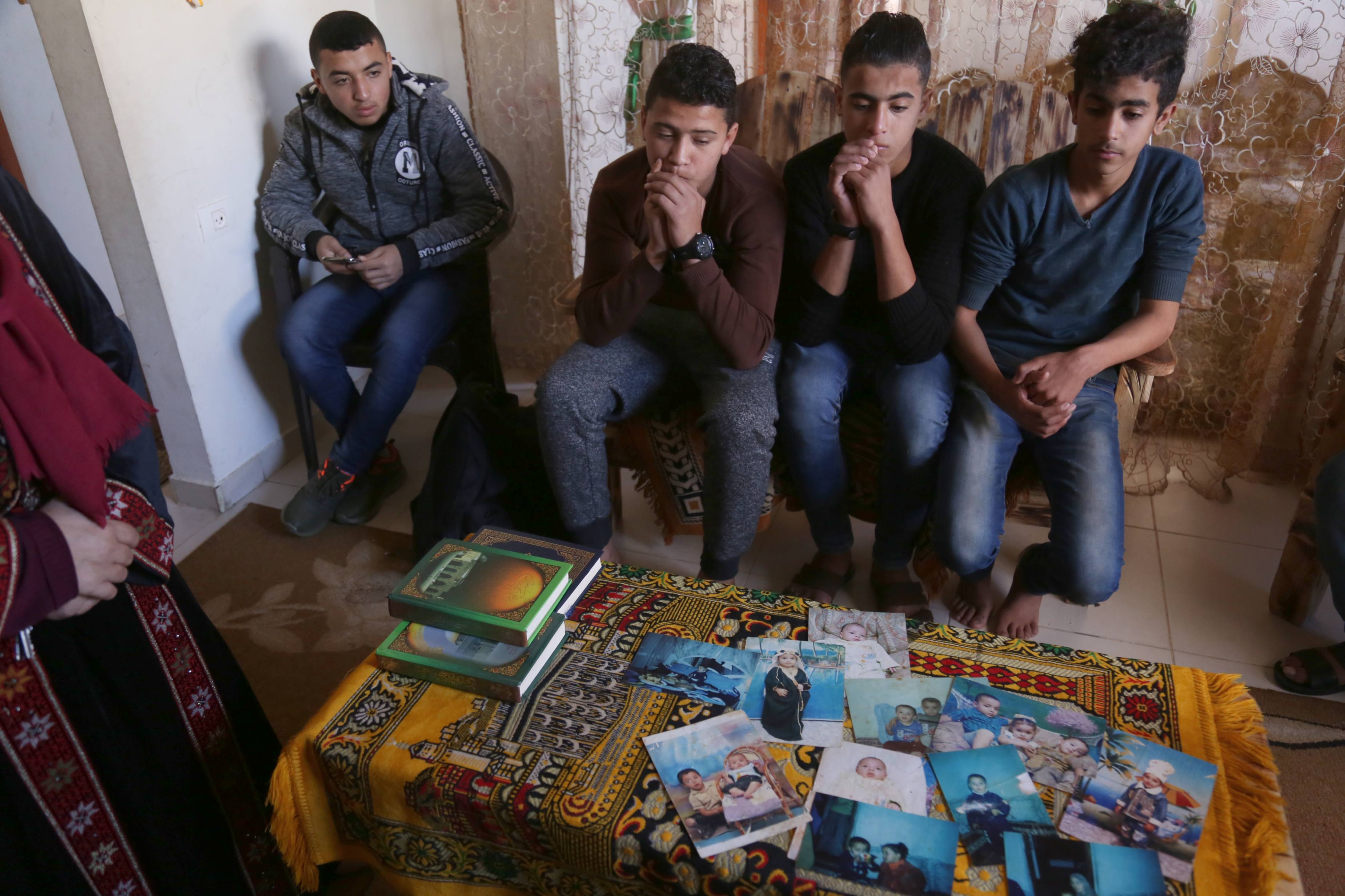 Abdel Fattah Shalabi, 16, Ahmed Abu Ramadan, 15, Rasmi Abu Sabala,16, and Ahmed Abu Qusai, 14, look at childhood pictures of Hassan (MEE/Samar Abu Elouf) 