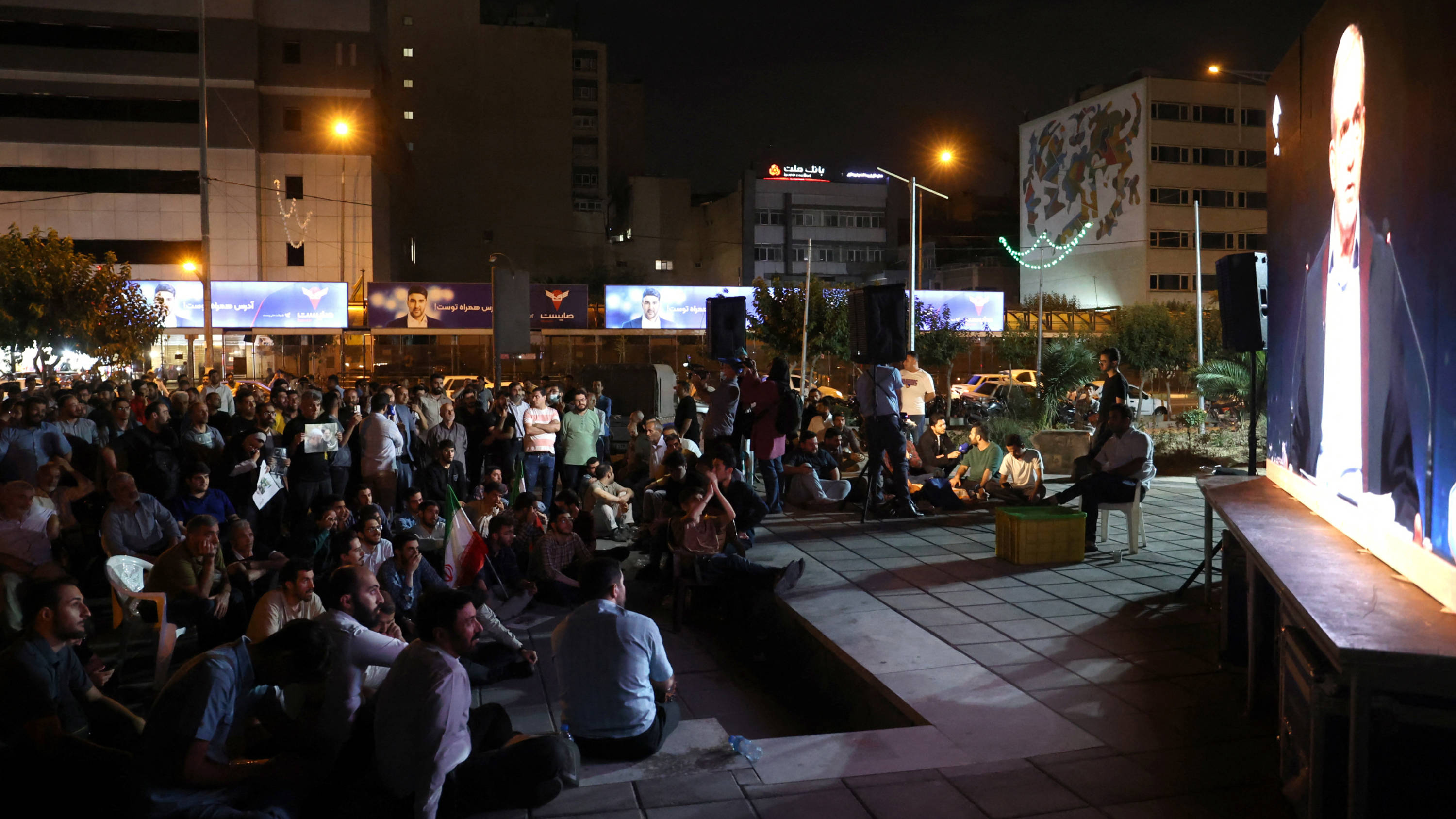 People watch the debate of presidential candidates at a park in Tehran, 1 July 2024 (WANA/Reuters)