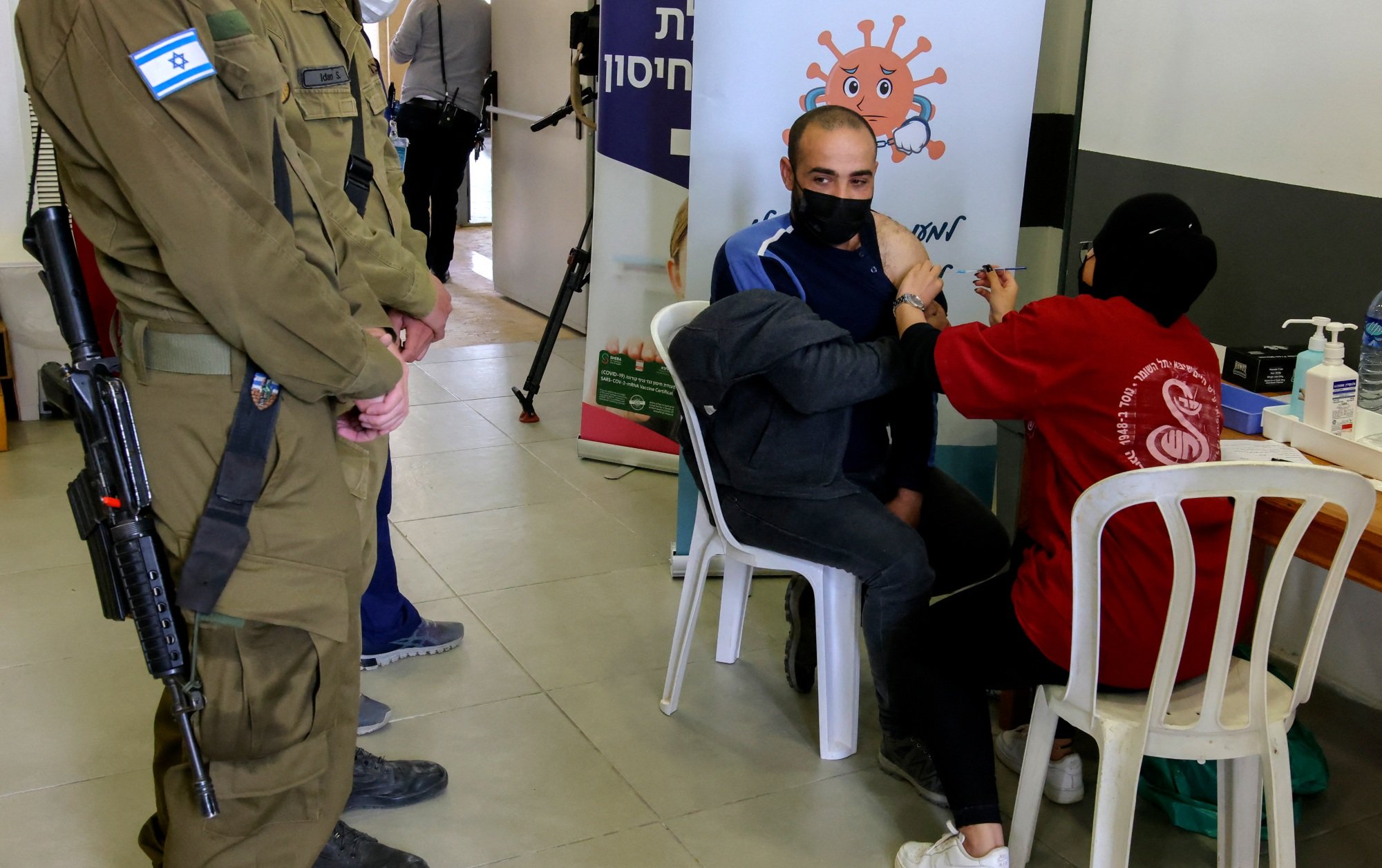 Une soignante israélienne administre le vaccin contre le COVID-19 à un Palestinien travaillant en Israël au check-point de Shaar Ephraim entre Israël et la Cisjordanie occupée près de Tulkarem, le 8 mars 2021 (AFP)