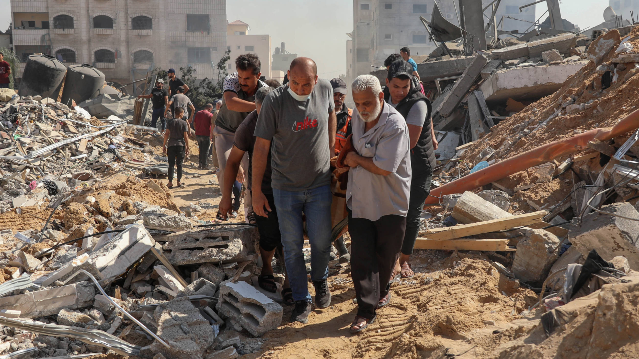 People transport a dead body after retrieving it from under the rubble of a building hit by an Israeli strike in al-Jalal street a day earlier, 26 October 2023 (MEE/Mohammed al-Hajjar)