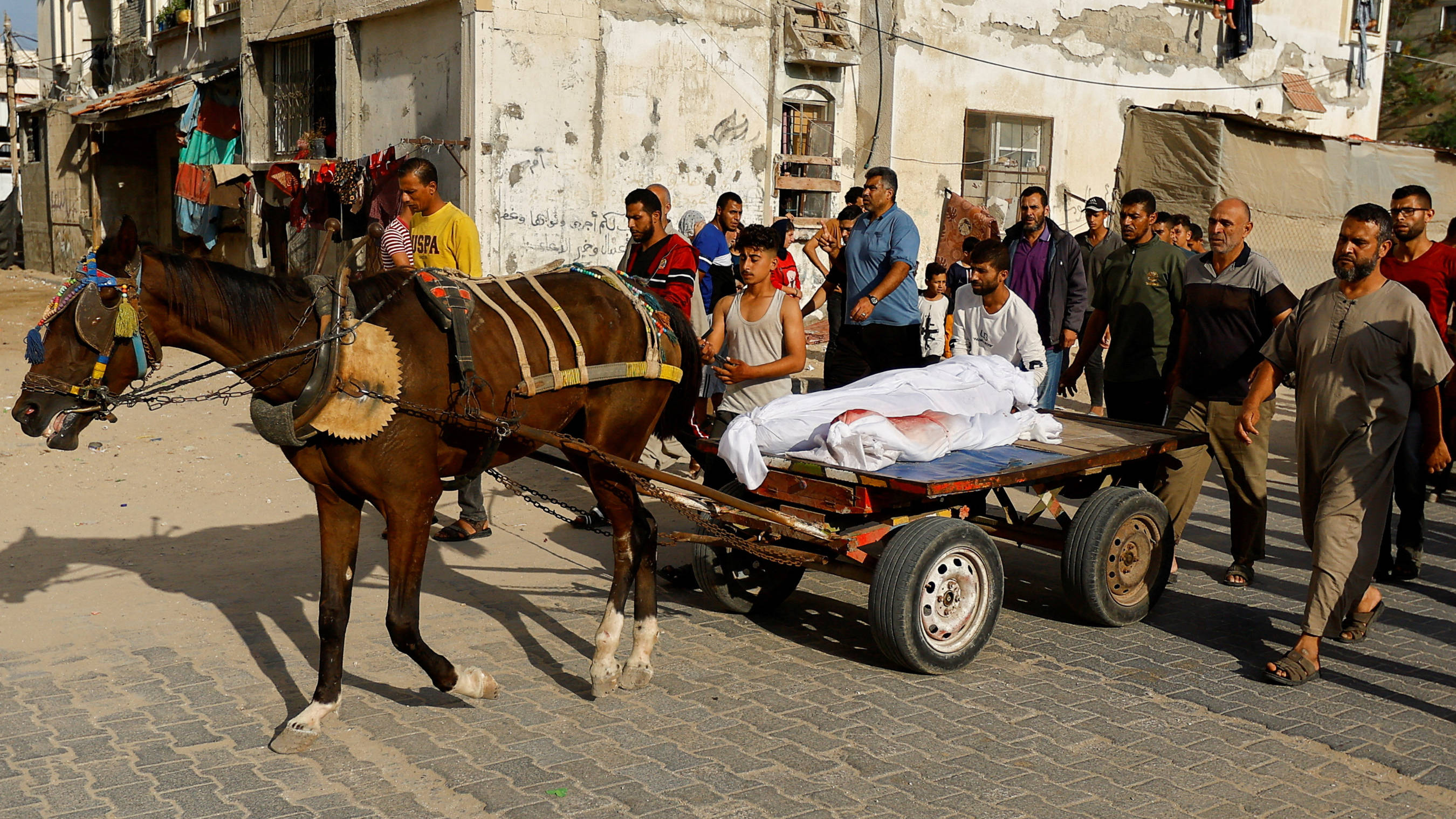 People transport the bodies of Palestinians, killed in Israeli strikes, on a horse-drawn cart, amid shortages of fuel, during their funeral in Khan Younis, 27 October 2023 (Reuters)