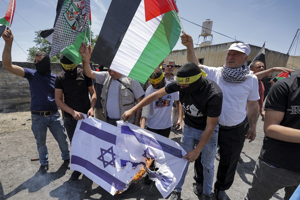 Des manifestants brandissent des drapeaux du Fatah et de la Palestine tout en brûlant des drapeaux israéliens lors d’une manifestation contre l’expropriation de terres palestiniennes par Israël dans le village de Kfar Qaddum (AFP)