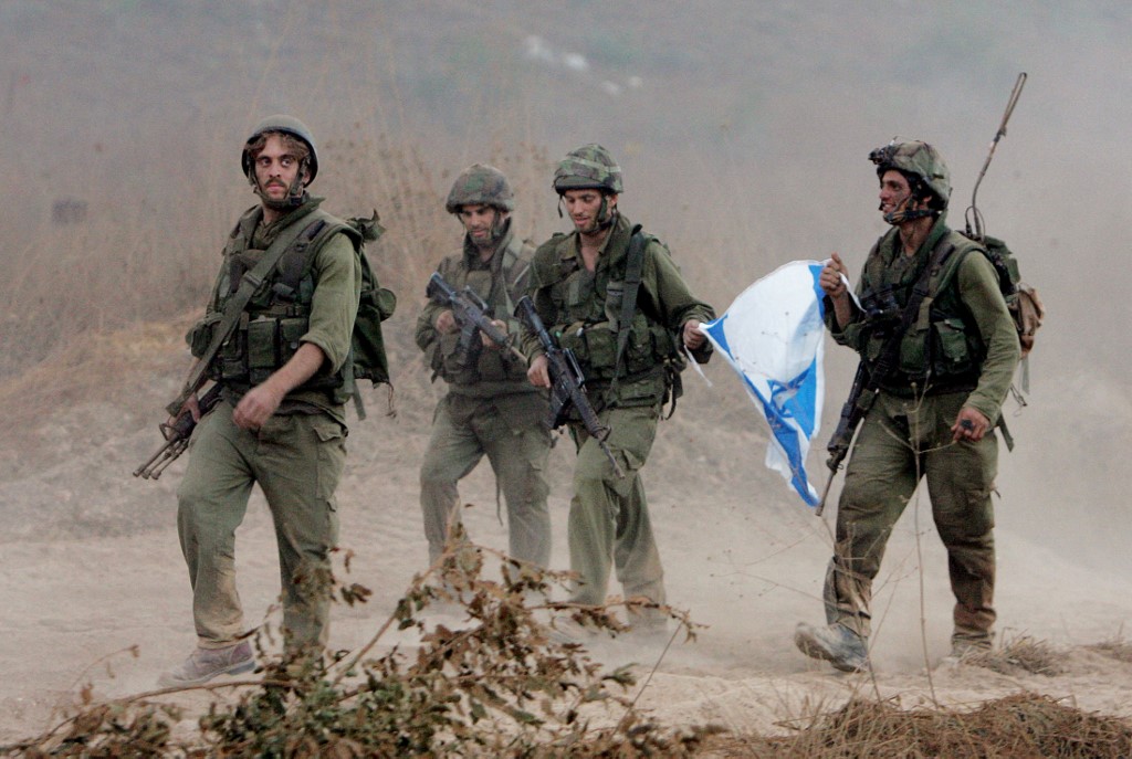 Israeli soldiers carry their national flag as they walk along the Israel-Lebanon border, 15 August 2006 (AFP)