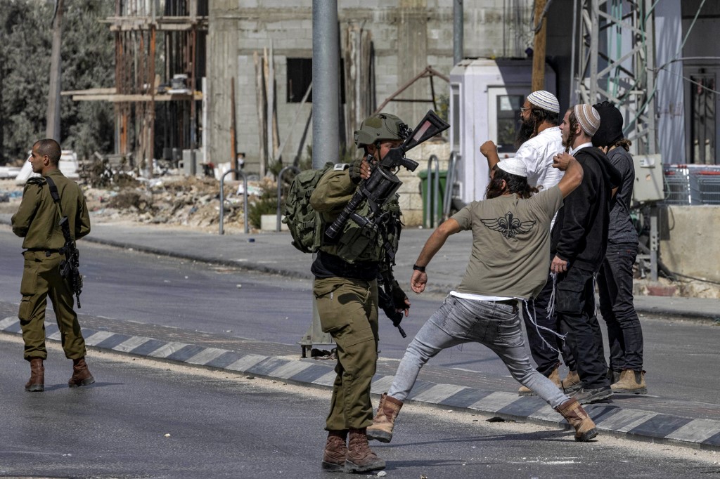 Israeli soldiers stand by as Israeli settlers throw stones at Palestinians (unseen) during clashes in the town of Huwara in the occupied West Bank on 13 October 2022 (AFP)