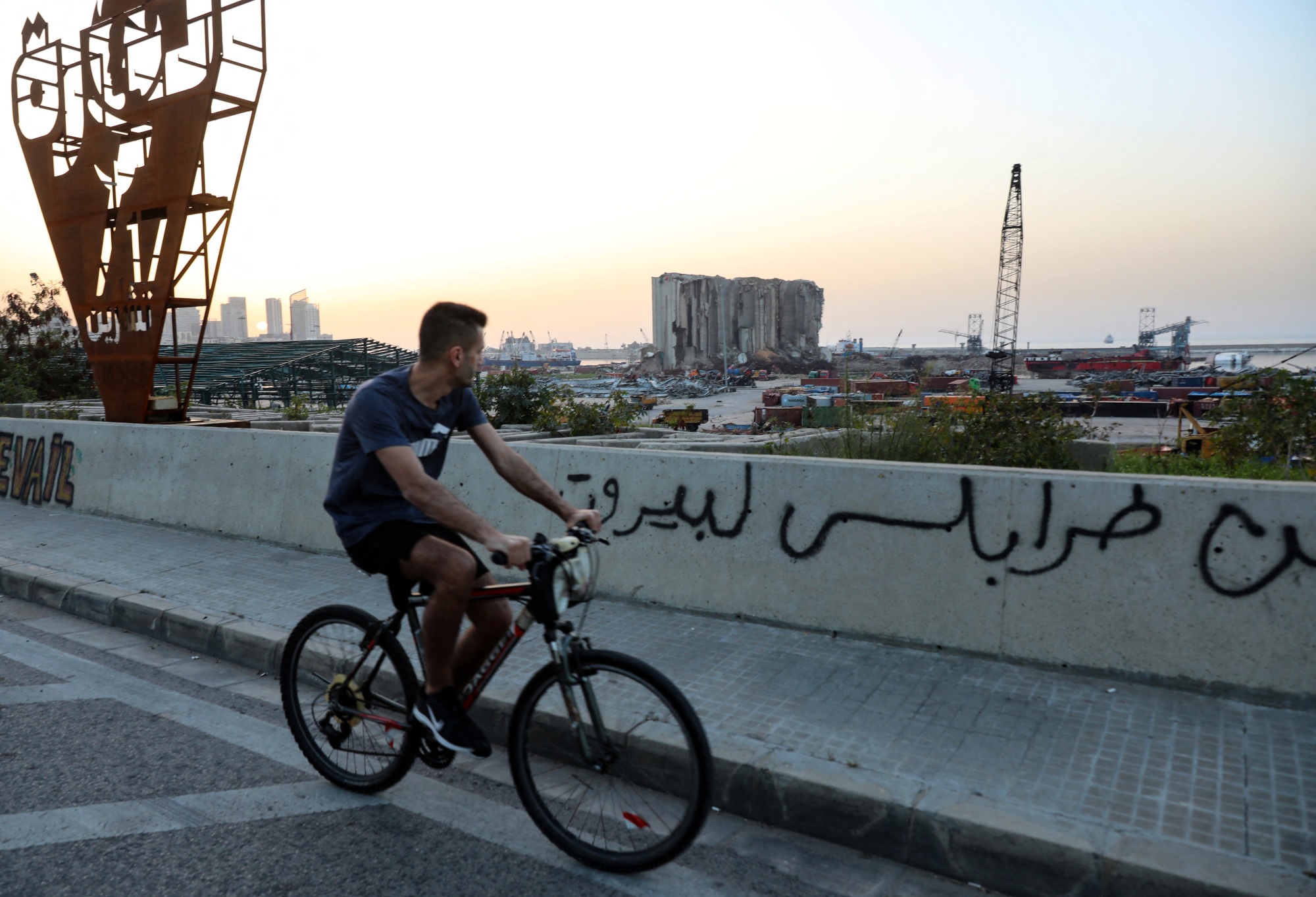 A young man on a bike stares at the destruction of the Lebanese capital Beirut's port as he drives past it on 6 April 2021 (AFP)