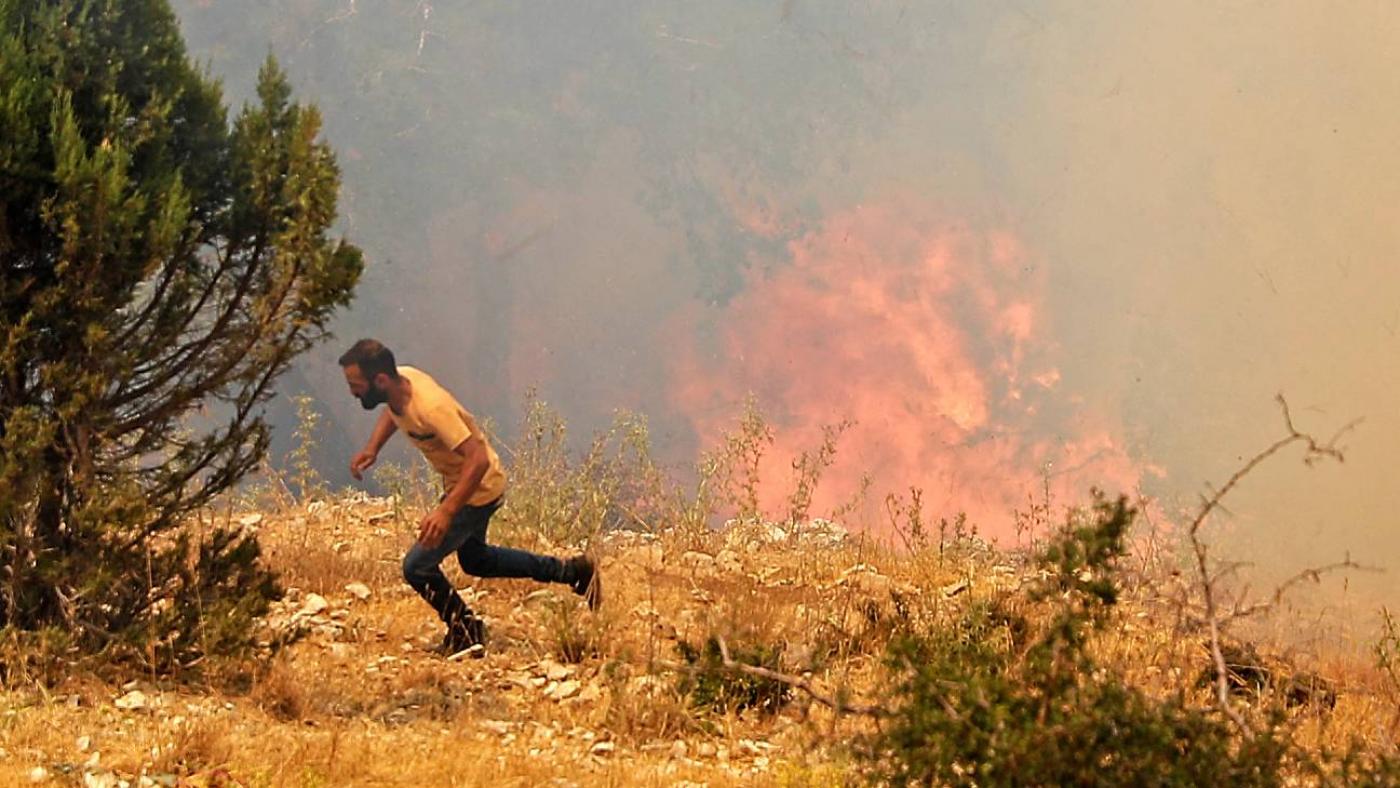 Un homme court se mettre à l’abri tandis que les pompiers éteignent un feu de forêt dans le nord du Liban dans le gouvernorat du Akkar, en juillet 2021 (AFP)