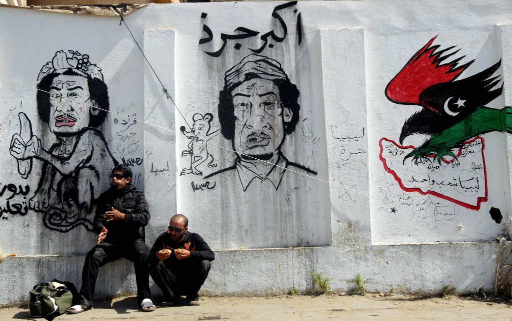 Libyan rebels eat lunch in front of a wall covered in graffiti mocking Libya's leader Moamer Kadhafi, in the rebel-held city of Benghazi, eastern Libya, 14 April 2011 (AFP)