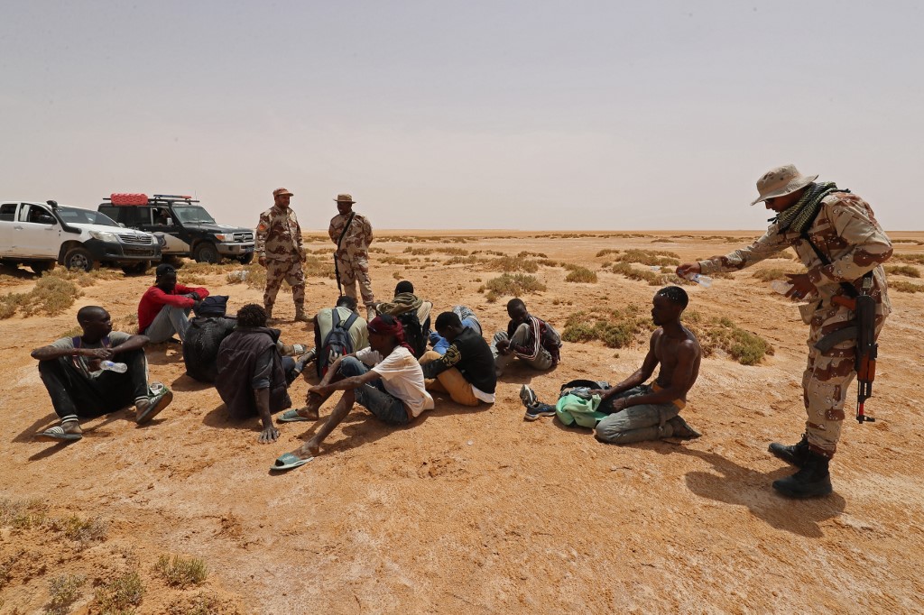 Libyan border guard assist people of African origin who reportedly have been abandoned by Tunisian authorities, following their arrival in an uninhabited area near Al-Assah on the Libya-Tunisia border on 30 July 2023 (Mahmud Turkia/AFP)