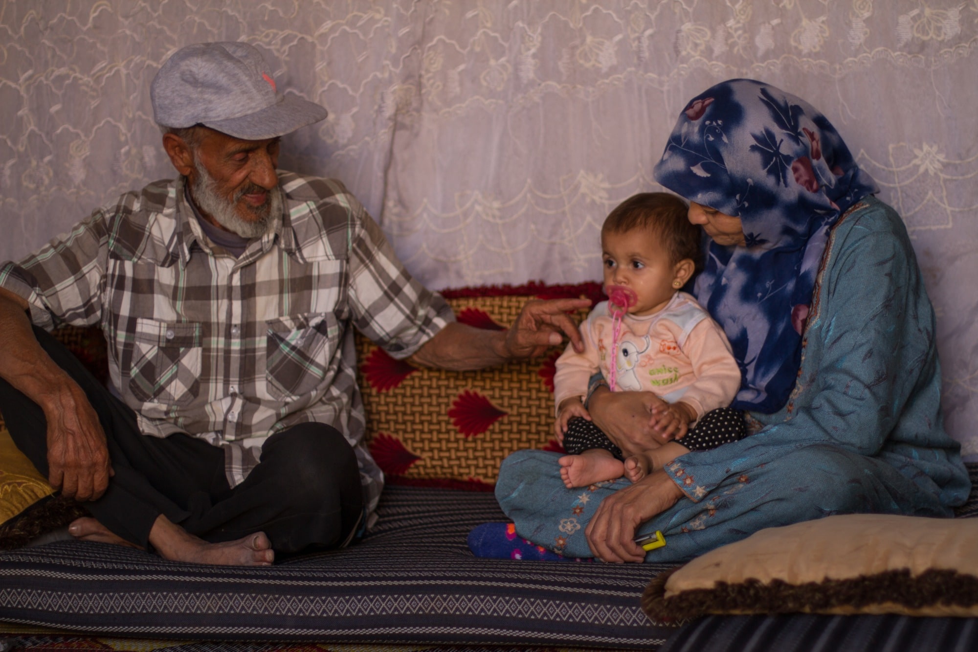 Abbas Nasser and his wife play with their grandchild in their tent in Syria's Idlib region (MEE/ Moawiya Atrash)