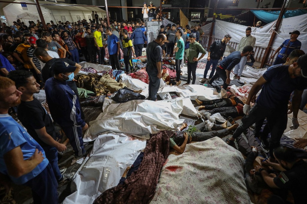 People gather around bodies of Palestinians killed after a strike ripped through the Ahli Arab hospital in central Gaza after they were transported to Al-Shifa hospital, on 17 October 2023 (AFP)