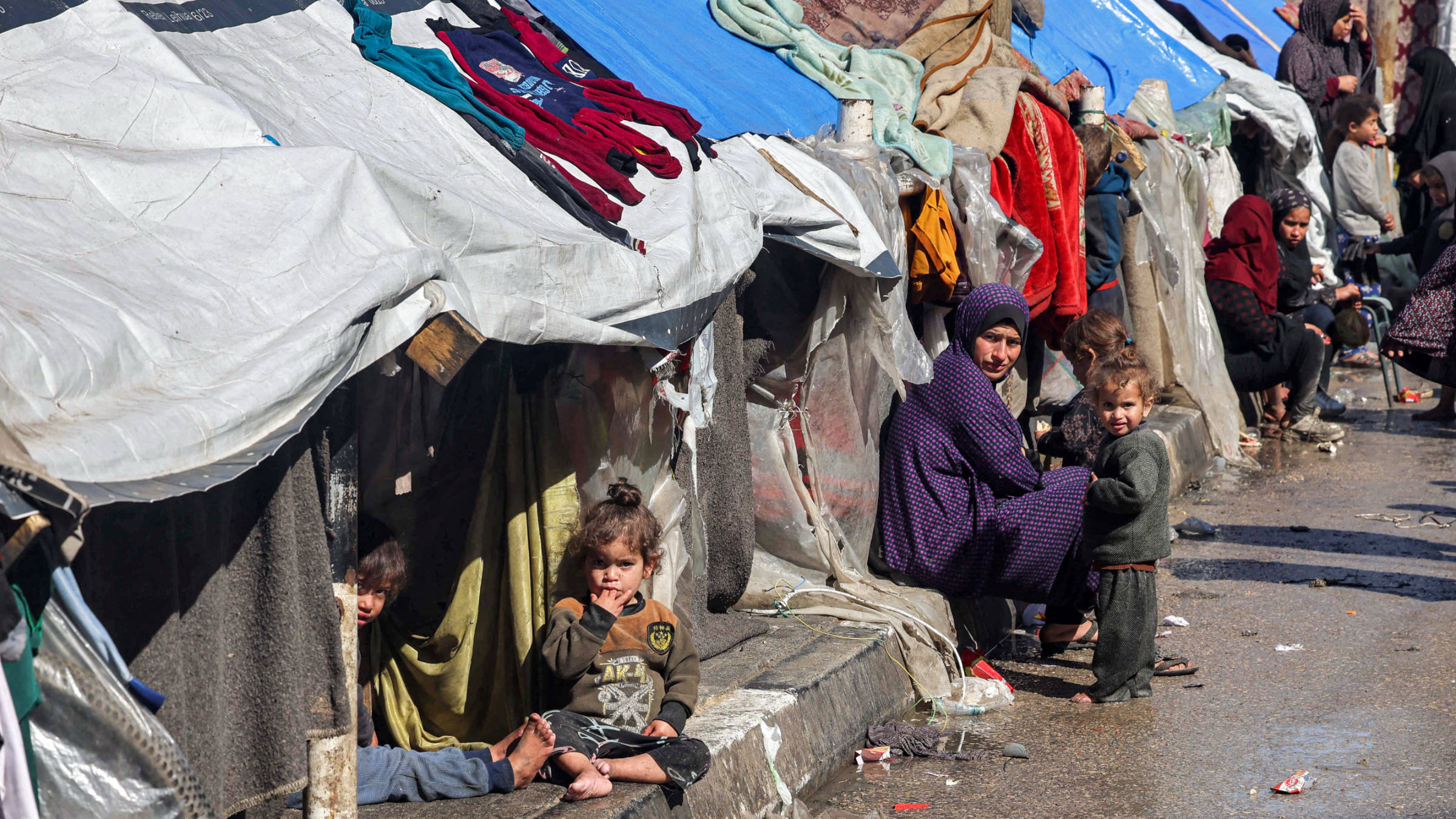 A woman and children sit outside tents sheltering displaced Palestinians in Rafah in the southern Gaza Strip on 8 February 2024 (AFP)