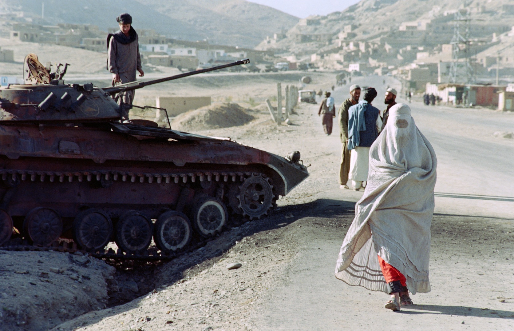 Une afghane fuit les zones de front en passant devant un véhicule blindé détruit appartenant aux forces de l’ex-gouvernement, à Kaboul le 30 octobre 1996 (AFP/ Saied Khan) 