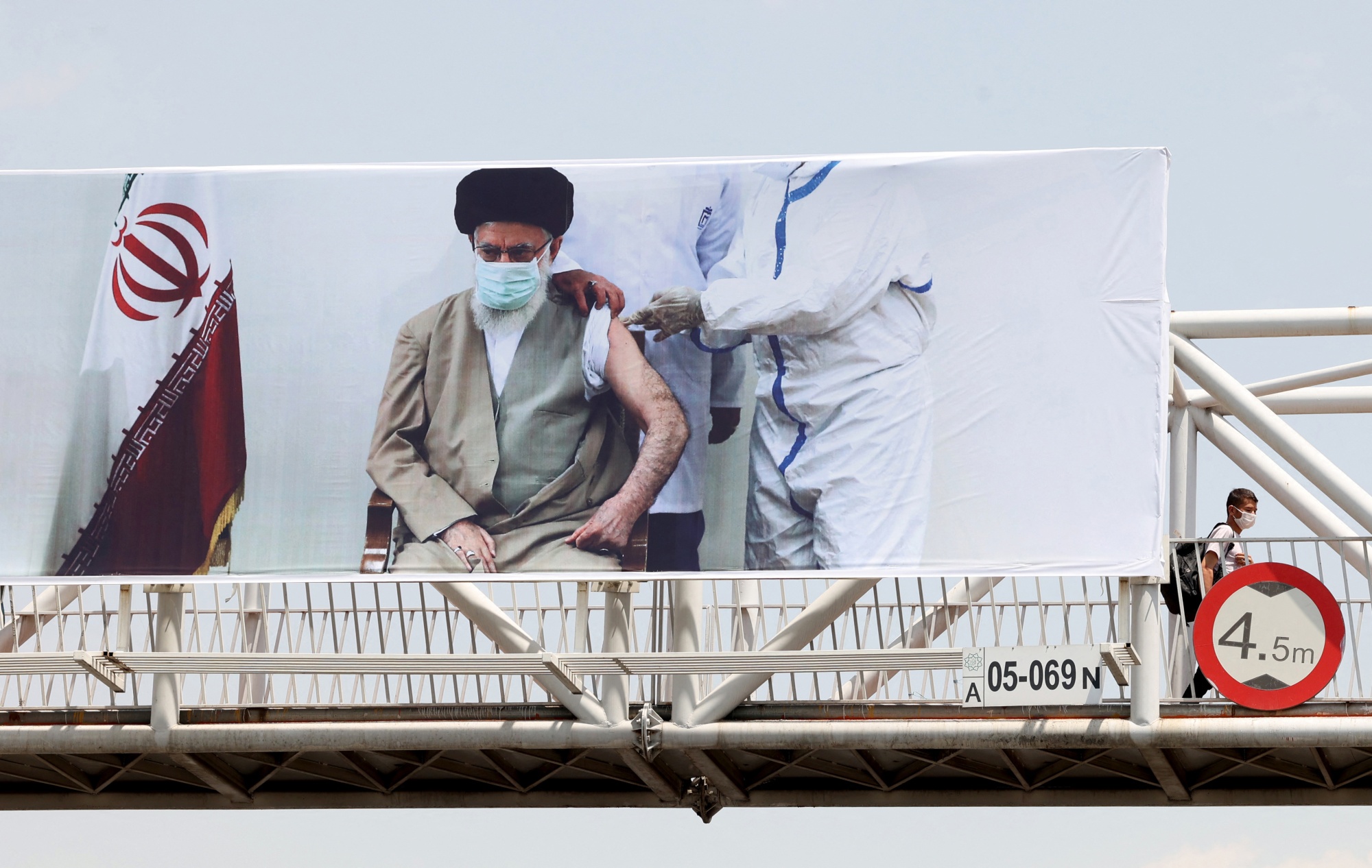 A man walks in front of a banner, showing Iran's supreme leader Ayatollah Ali Khamenei receiving a vaccine against the coronavirus, in the capital Tehran on 3 July 2021 (AFP)