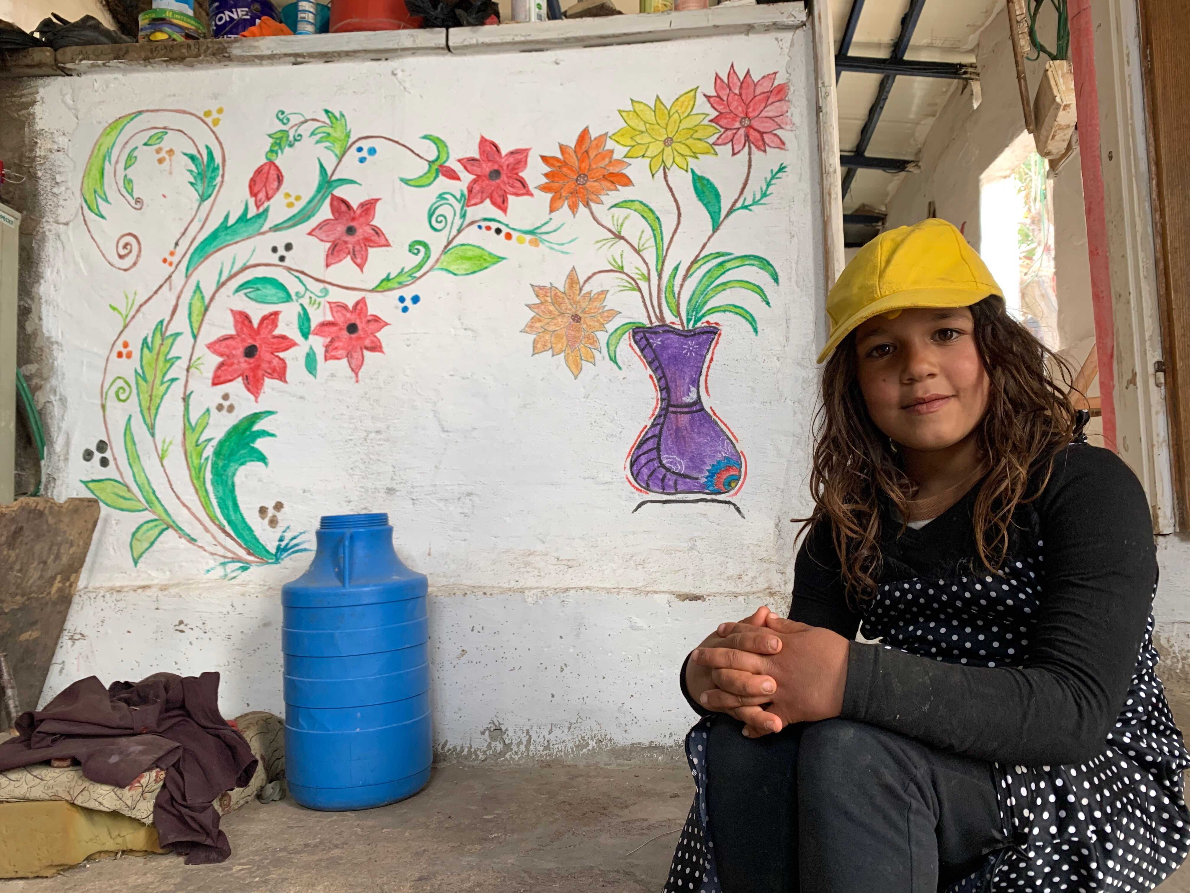 Maram, 8, poses in front of a colourful wall inside her family's home painted by her sister Rania (MEE/Shatha Hammad)