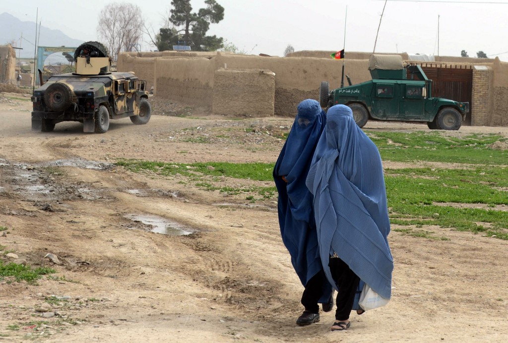 Des Afghanes marchent devant des véhicules blindés afghans fournis par l’Occident à Kandahar, le 3 avril 2014 (AFP)