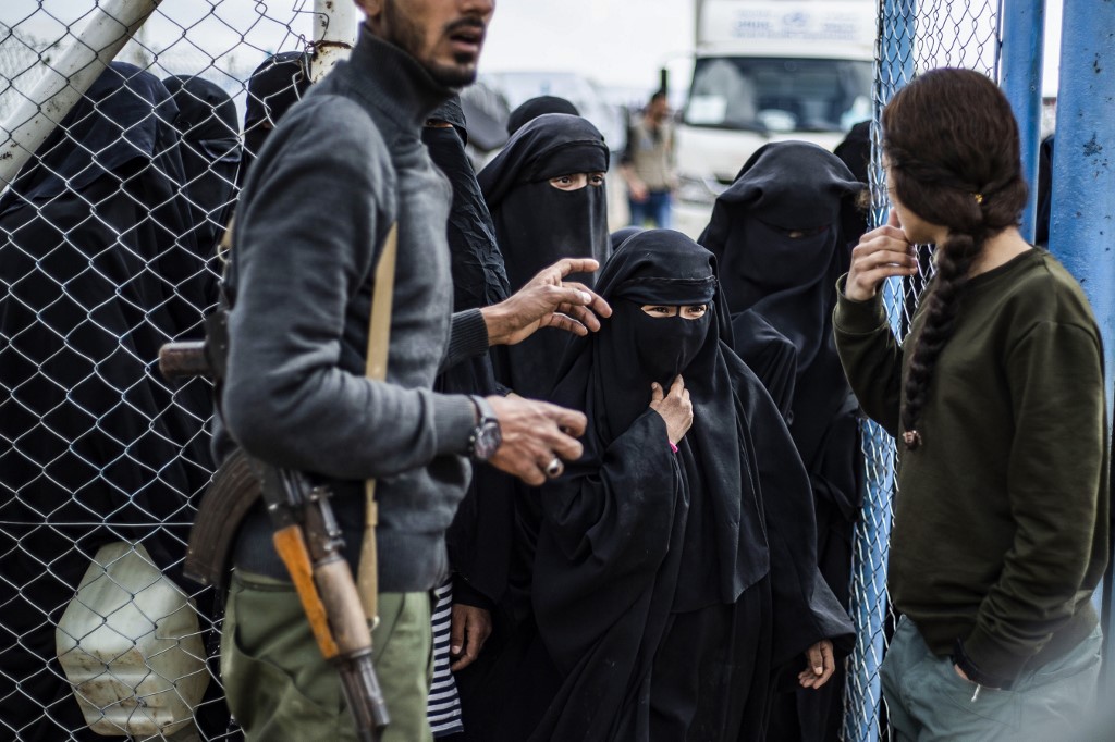 Des membres des FDS montent la garde pendant que des femmes passent une clôture à al-Hol (AFP)