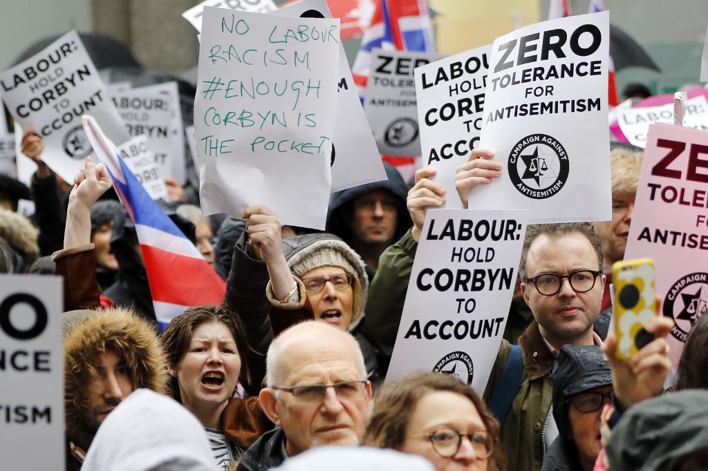In this file photo taken on April 08, 2018 people hold up placards and Union flags as they gather for a demonstration organised by the Campaign Against Anti-Semitism outside the head office of the British opposition Labour Party
