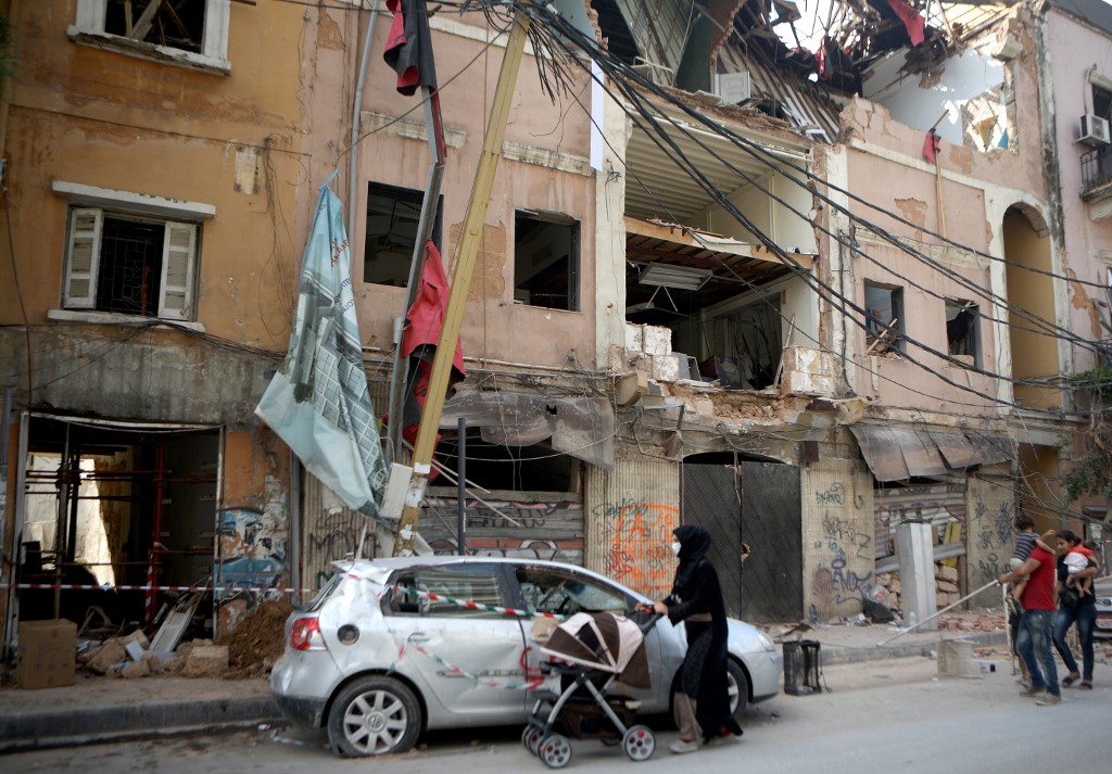 Syrian refugees walk past damaged buildings in the partially destroyed Beirut neighbourhood of Mar Mikhael on 13 August after the city’s massive port explosion (AFP)