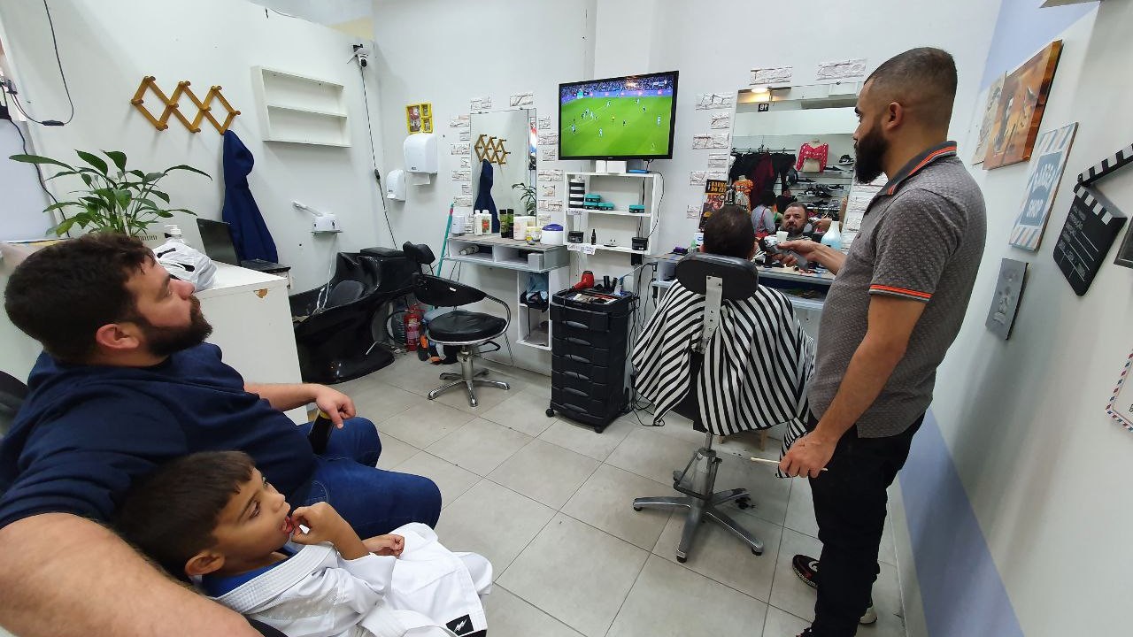 Locals come to Taha Yasin's barbershop to get a haircut and also watch the football (MEE/Eman Abusidu)
