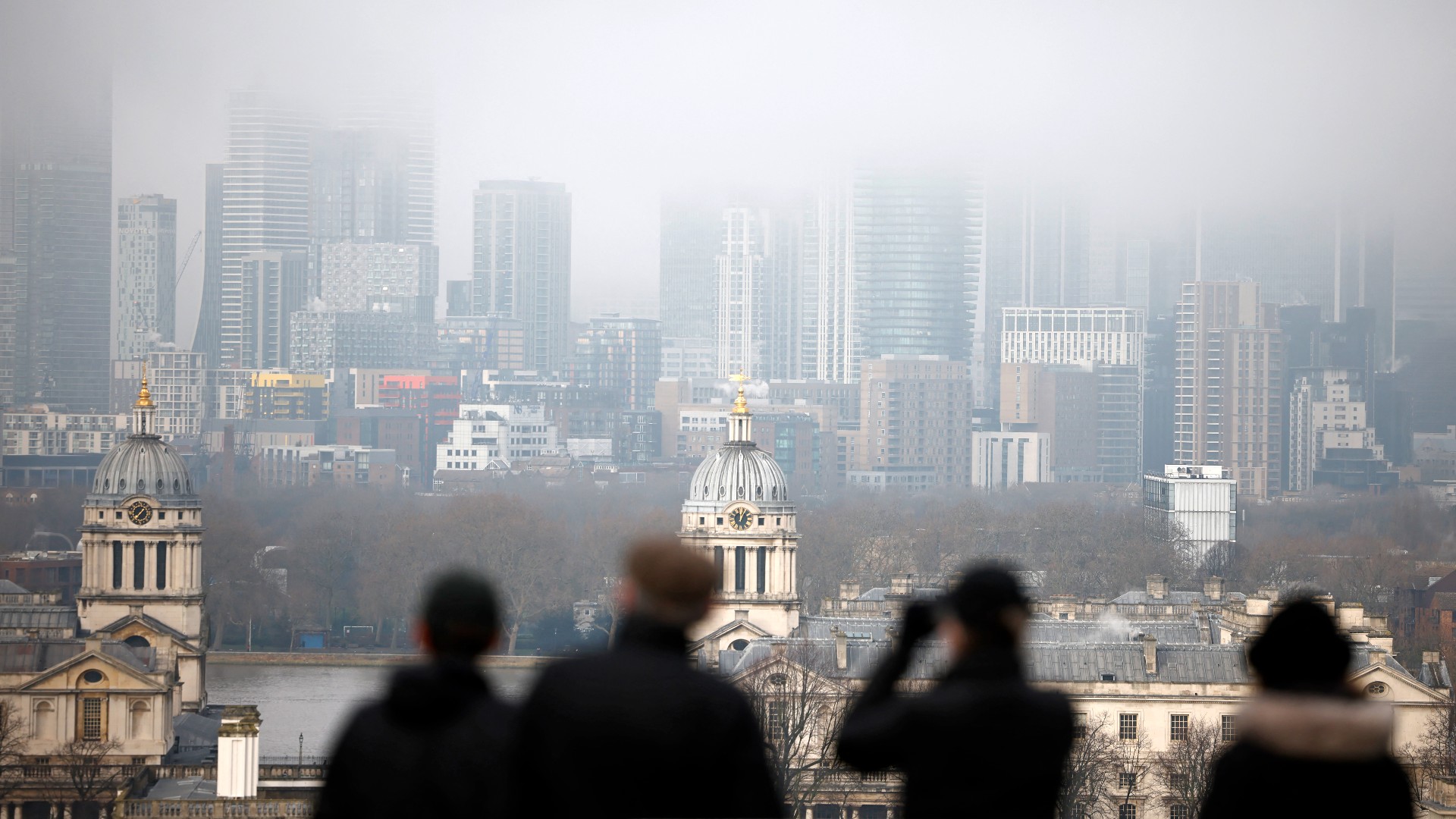 People walk in Greenwich Park with the office buildings of the Canary Wharf financial district in the background in London on the bank holiday, December 28, 2020