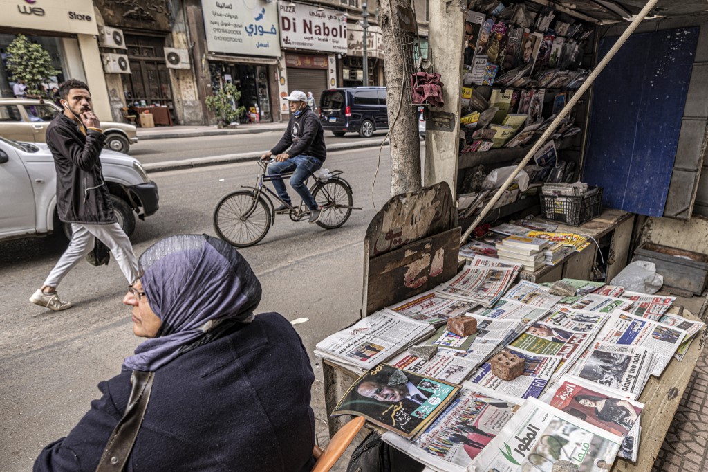 A woman sits in a chair next to newspapers on display at a newsstand along Kasr al-Aini street in the centre of Egypt's capital Cairo on February 17, 2022. 