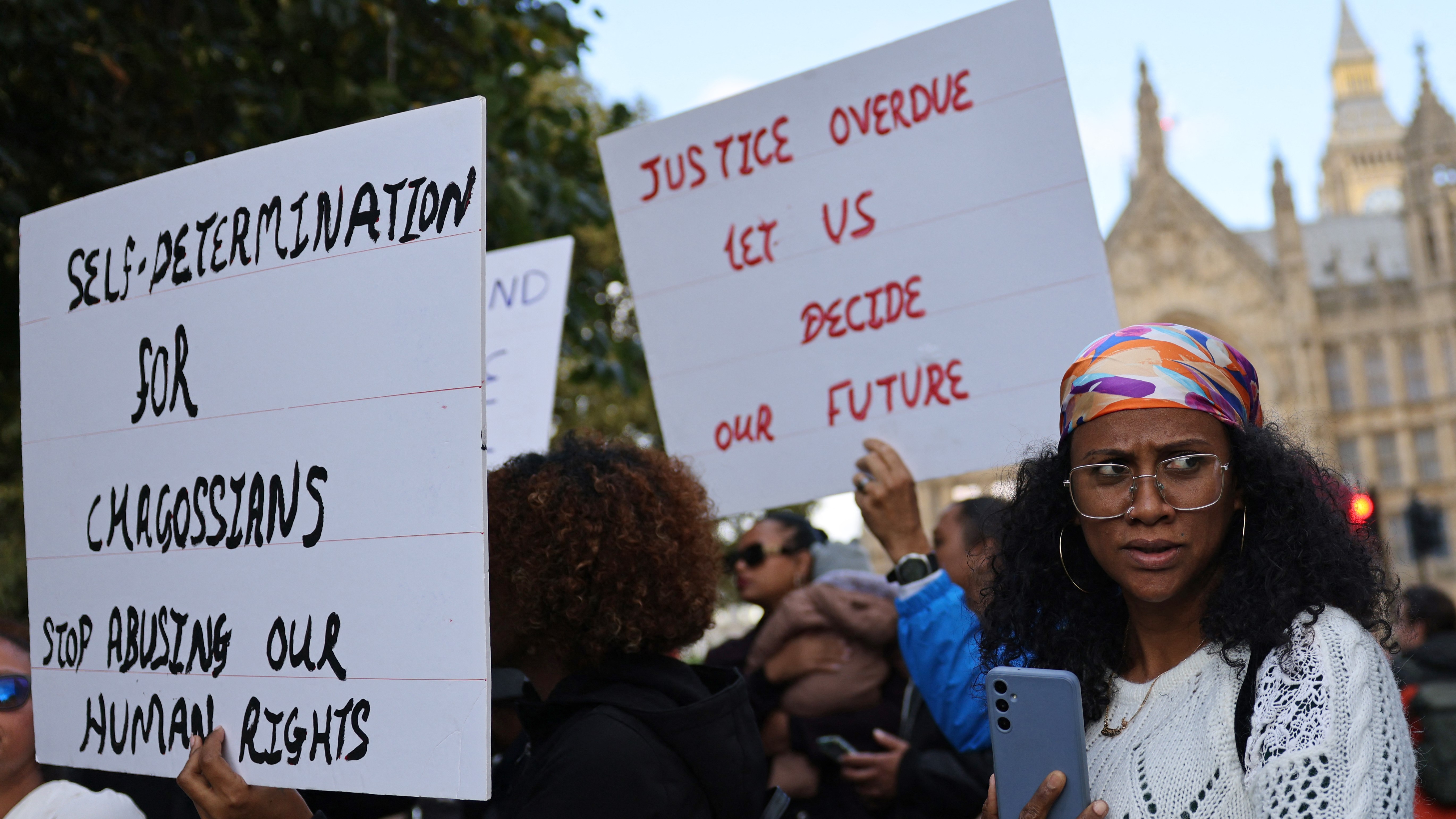 Members of the Chagossian community gather with banners and placards outside parliament to protest against being left out of negotiations on 7 October (AFP)