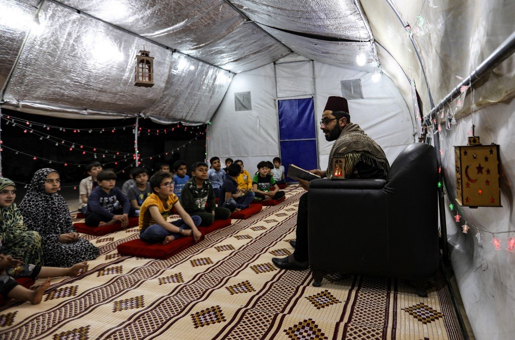 Des enfants syriens écoutent un conteur traditionnel dans un camp pour personnes déplacées dans la province d’Idleb, dans le nord-ouest du pays, le 29 avril 2021 (AFP)
