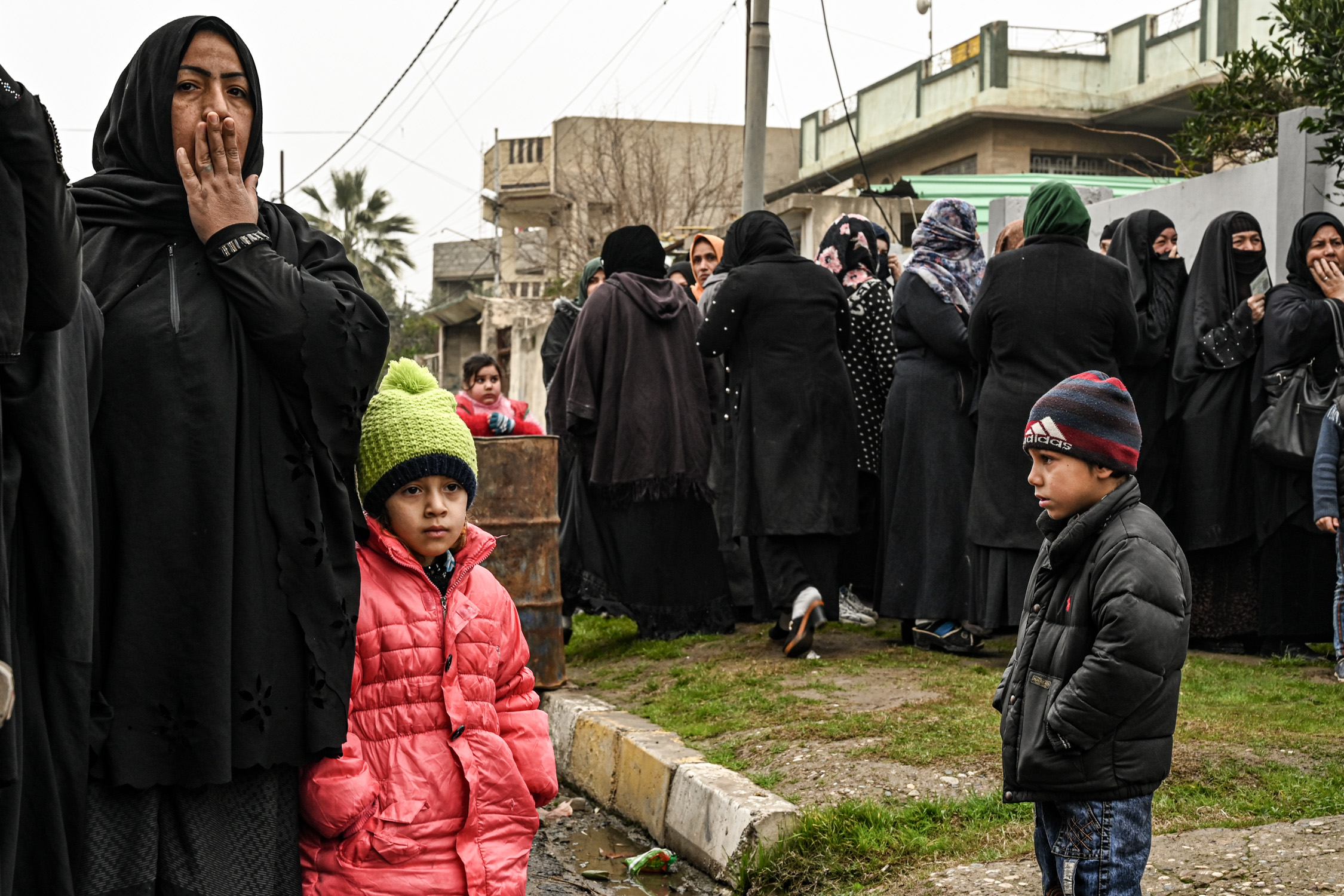 A woman waits with her children to receive aid at a handout in Mosul (MEE/Finbar Anderson)
