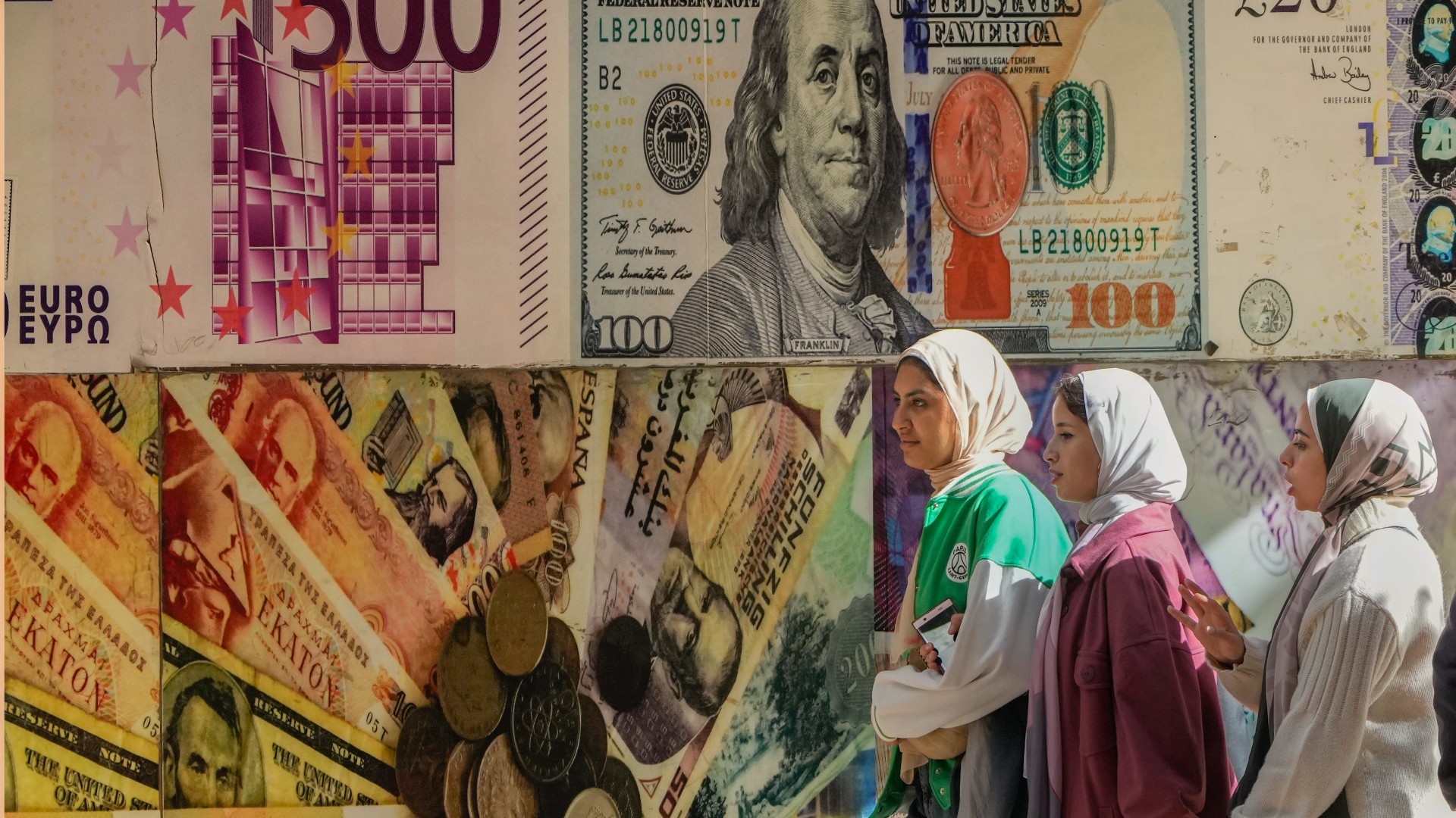 Egyptians walk past a poster depicting U.S. dollars and other currencies outside an exchange office in Cairo, Egypt, Thursday, Jan. 12, 2023.