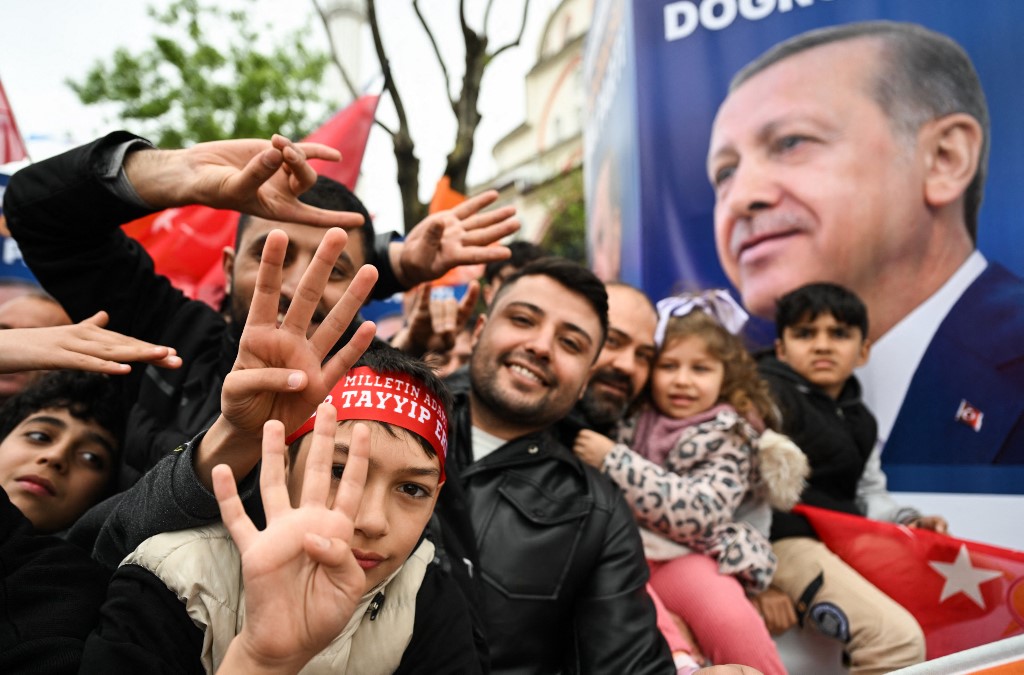 Des partisans d’Erdoğan font le signe des quatre doigts de Rabia à côté d’un portrait du président lors d’un meeting de campagne à Istanbul, le 12 mai 2023 (AFP)