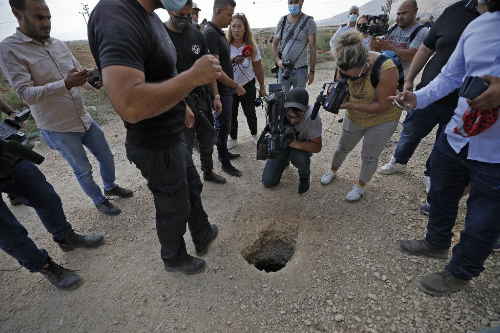 Police and journalists gather around a hole used by six Palestinians to escape from Gilboa prison in northern Israel on 6 September 2021 (AFP)