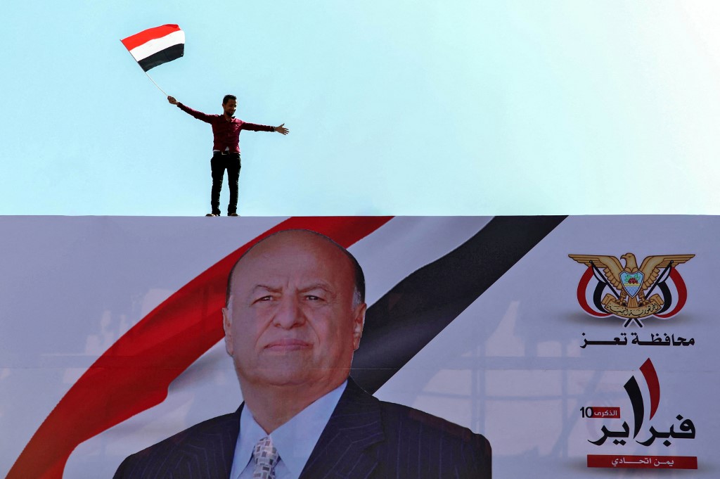 A Yemeni youth waves a national flag atop a billboard of President Abd Rabbuh Mansour Hadi in Taiz on 11 February 2021 (AFP)