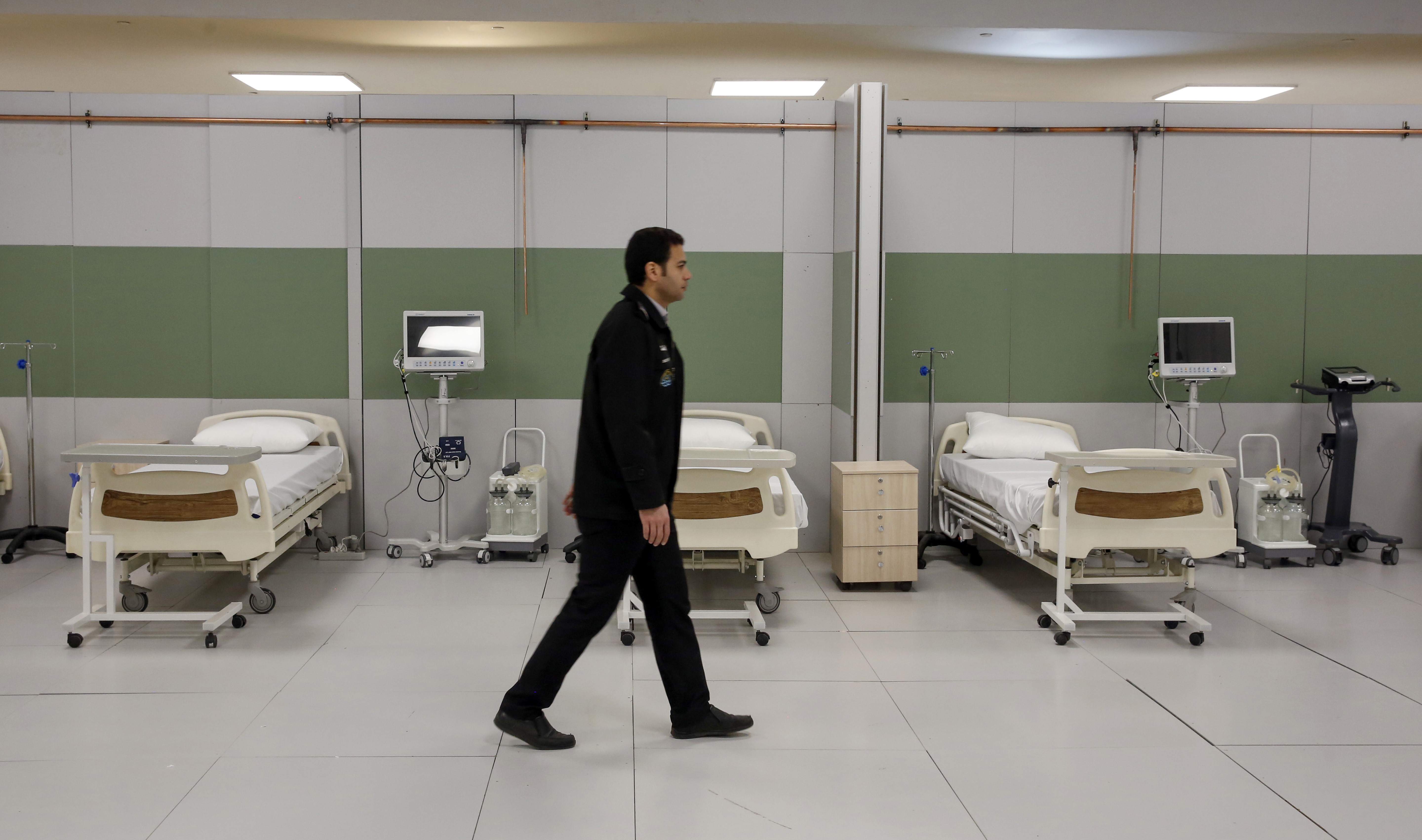An Iranian worker walks past beds at a makeshift hospital inside the Iran Mall, northwest of Tehran, on 21 March (AFP)
