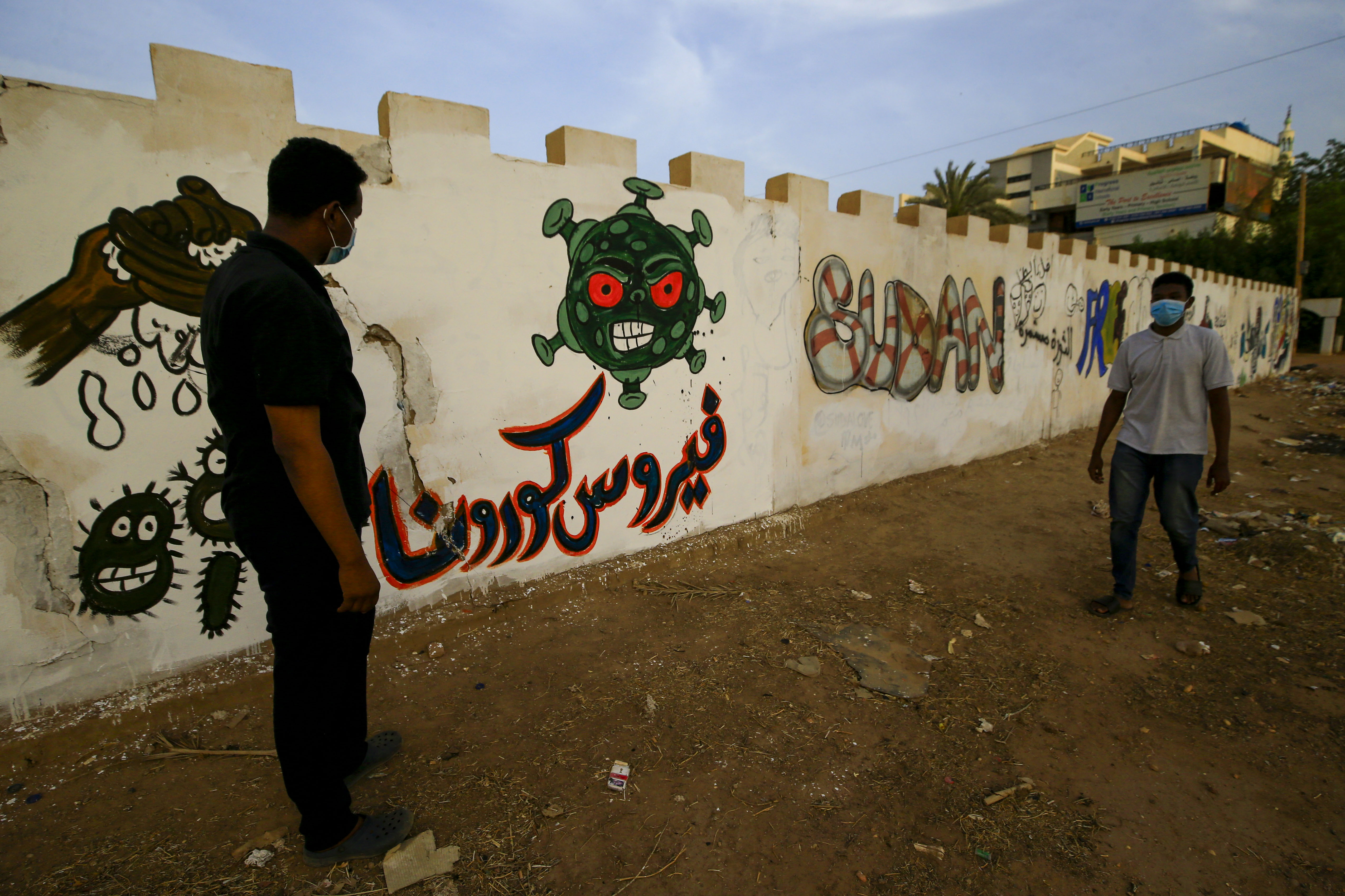 Sudanese volunteers stand next to graffiti of the Covid-19 virus in the capital Khartoum on 8 April as they clean a street (AFP)