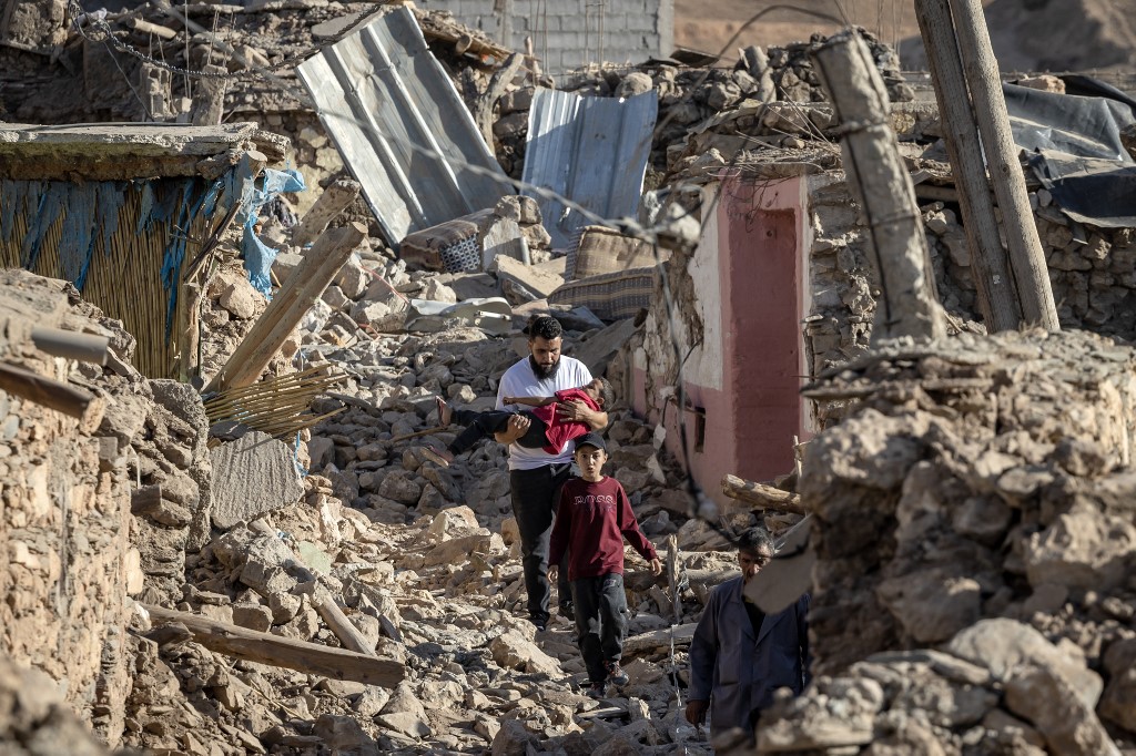 People walk past destroyed houses after an earthquake in the mountain village of Tafeghaghte, southwest of the city of Marrakesh, on September 9, 2023. 