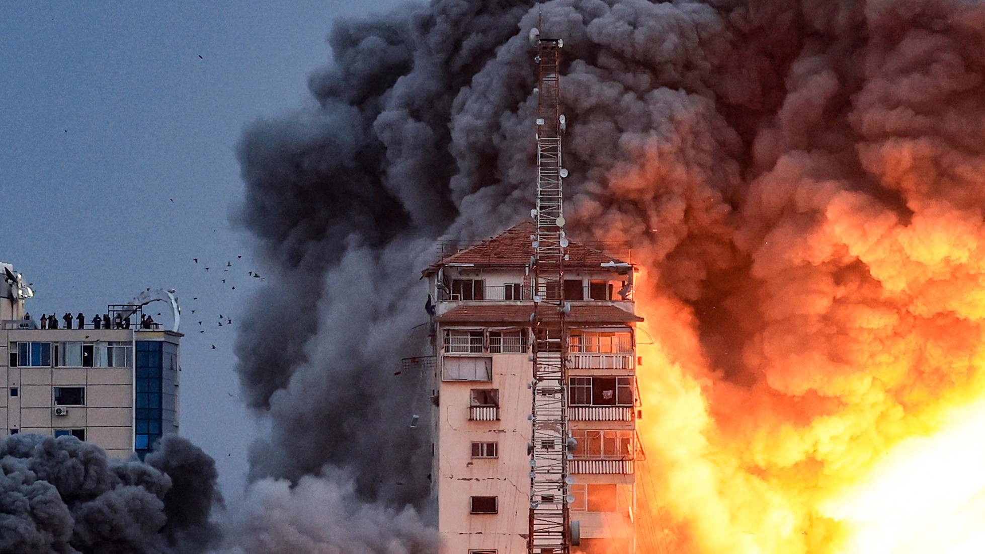 People standing on a rooftop watch as a ball of fire and smoke rises during an Israeli air strike that hit the Palestine Tower building (AFP)